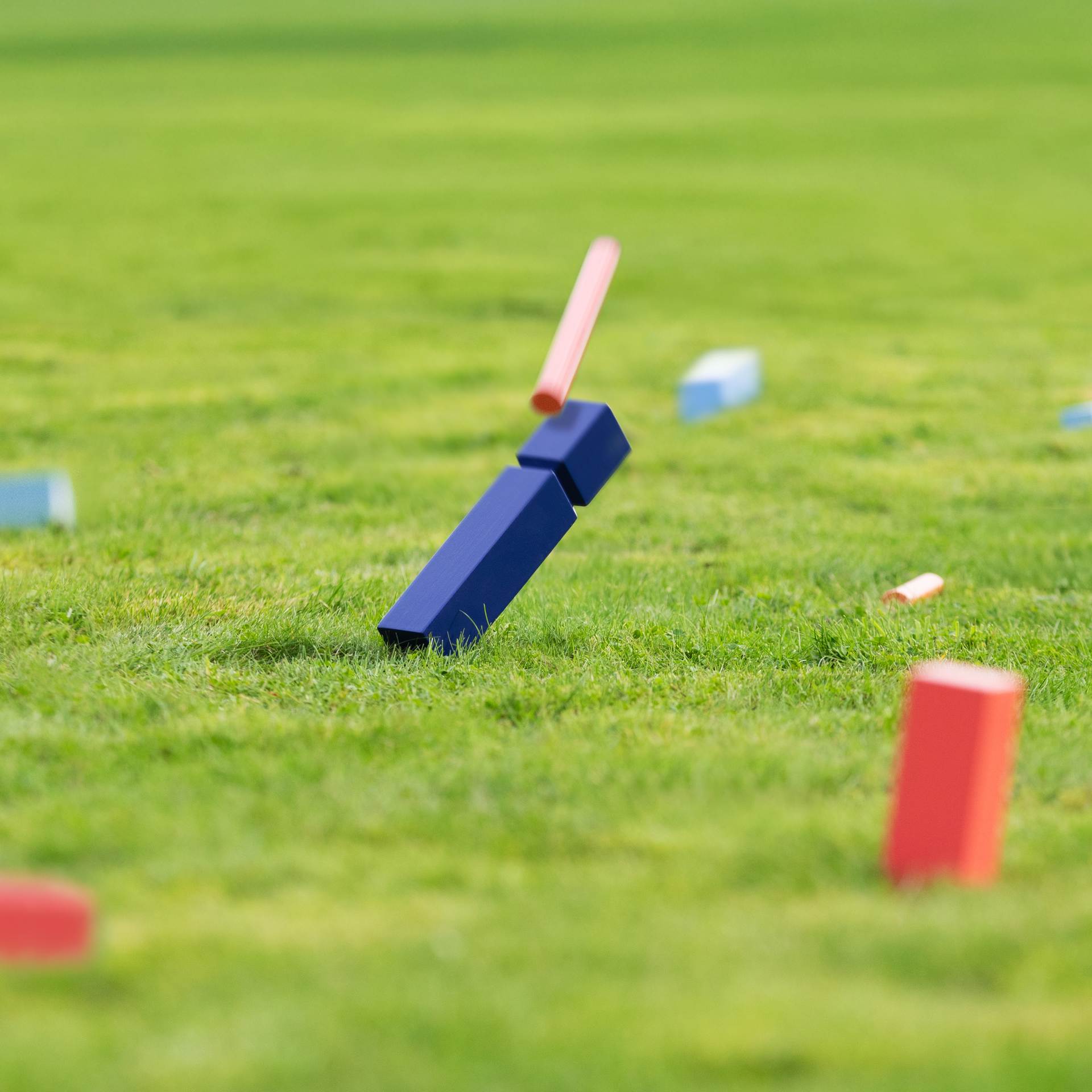 Holzspiel Kubb: blaue und rote Spielsteine, ein großer, blauer König, orangefarbene Wurfstäbe und hellblaue Eckstäbe sind aufgereiht.