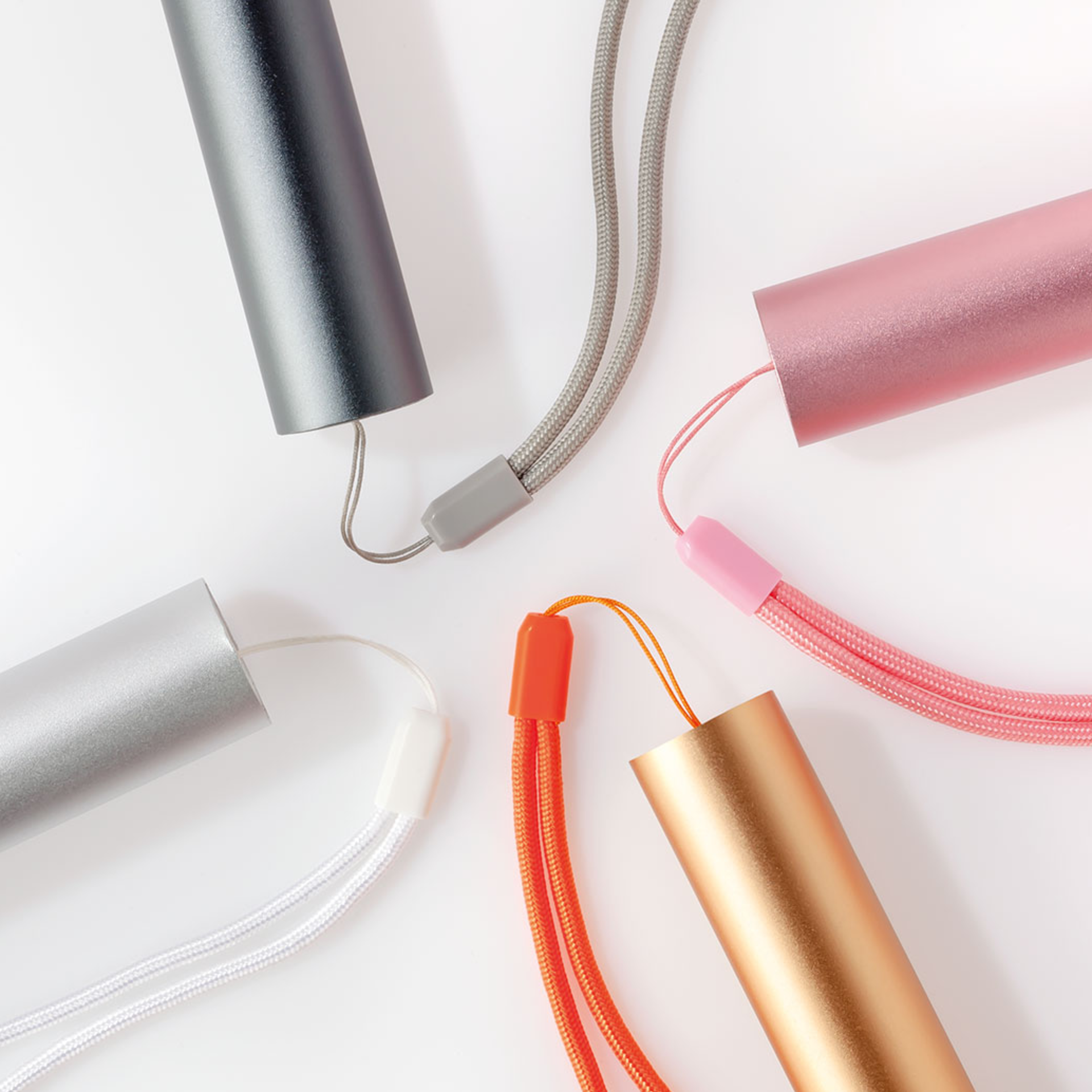 Fünf Akku-Ventilatoren in Silber, Grau, Gold, Rosa und Orange mit farblich passenden Handschlaufen liegen kreisförmig auf weißem Grund.