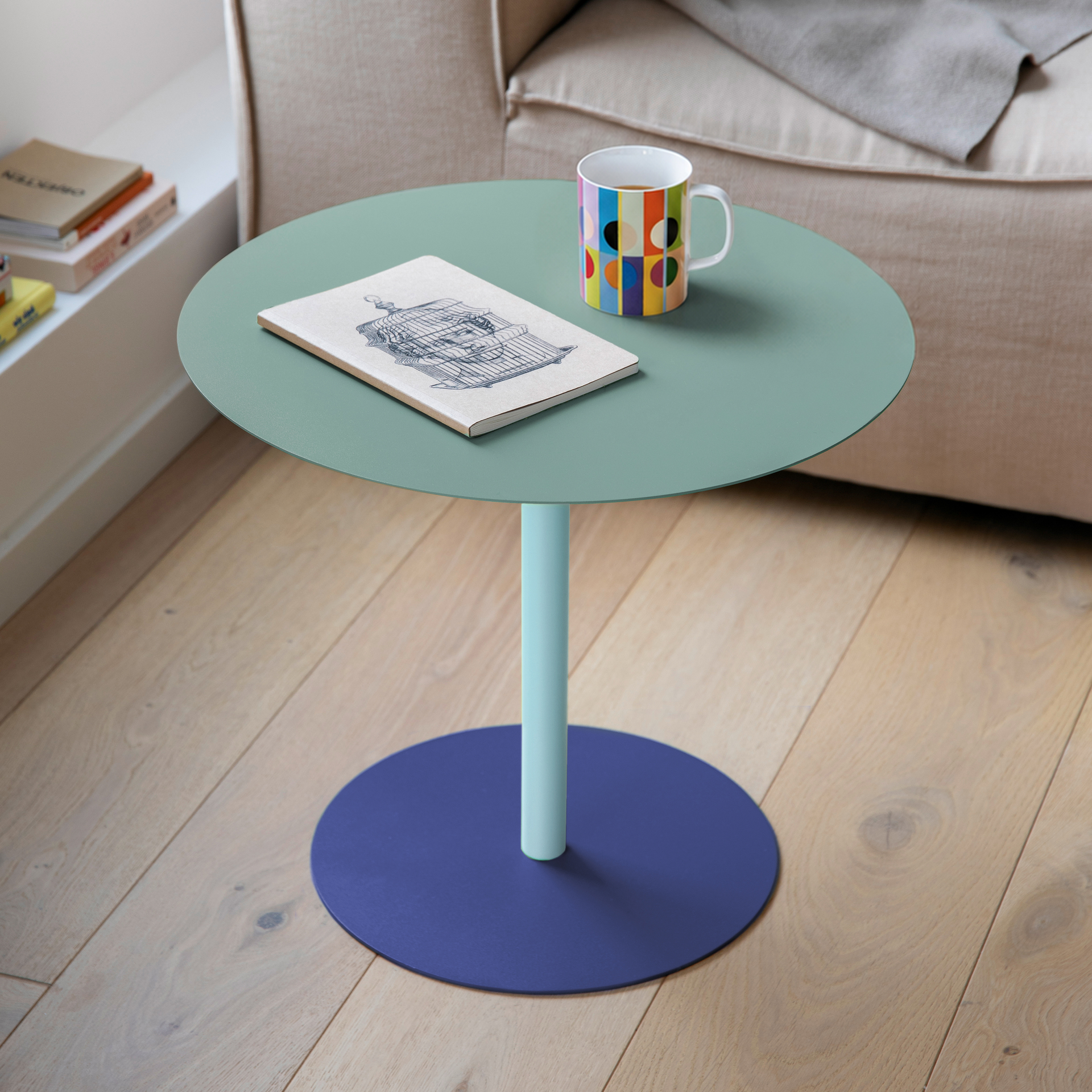 Table d'appoint moderne aux formes arrondies. Plateau vert menthe sur pied cylindrique bleu clair, posé sur une base ronde stable bleu foncé. Couleurs ciel et mer, idéale comme support élégant.
