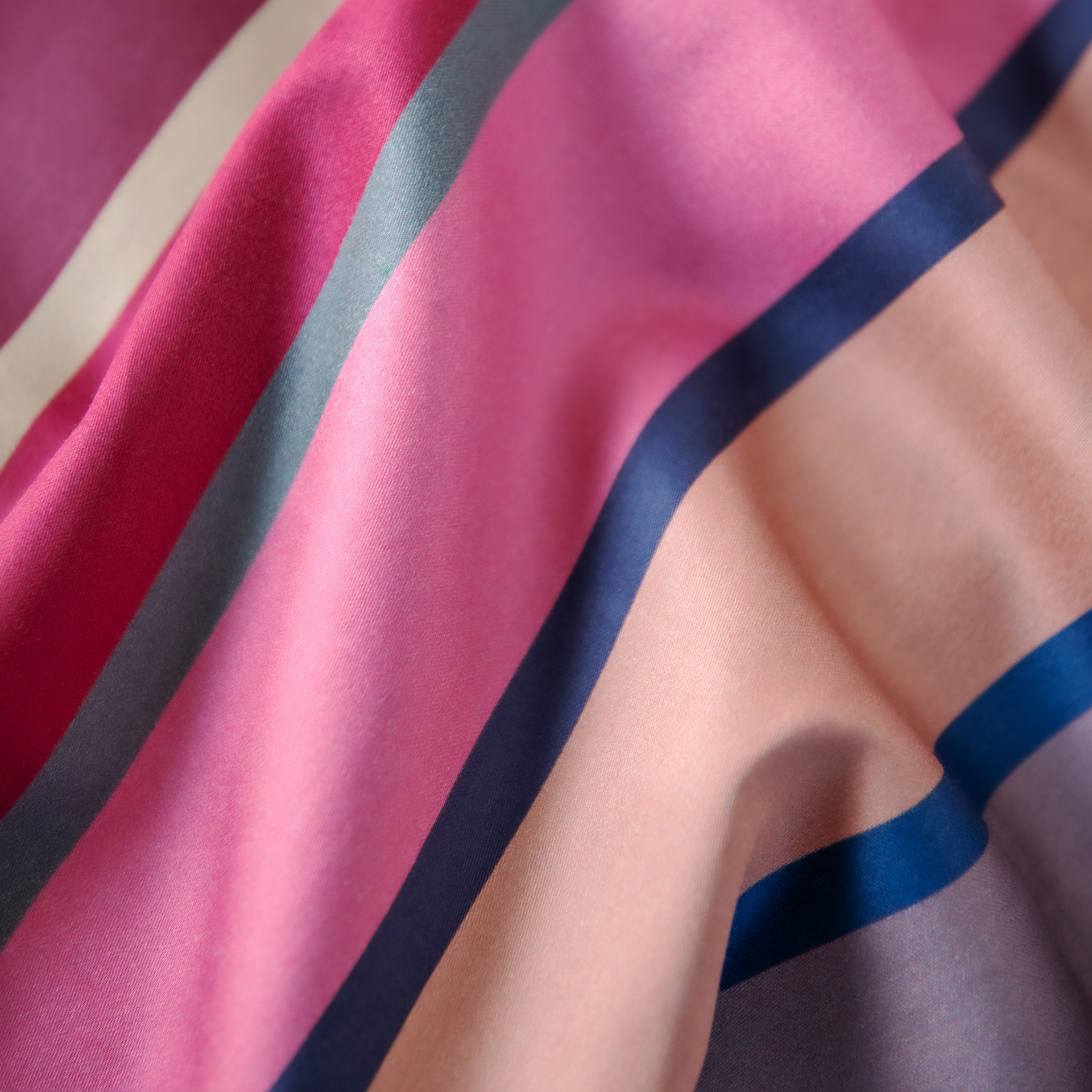 Detailaufnahme der Mako-Satin-Bettwäsche 'Ascona' mit pinken, roten, grauen und beigen Streifen. Stoff leicht gewellt.