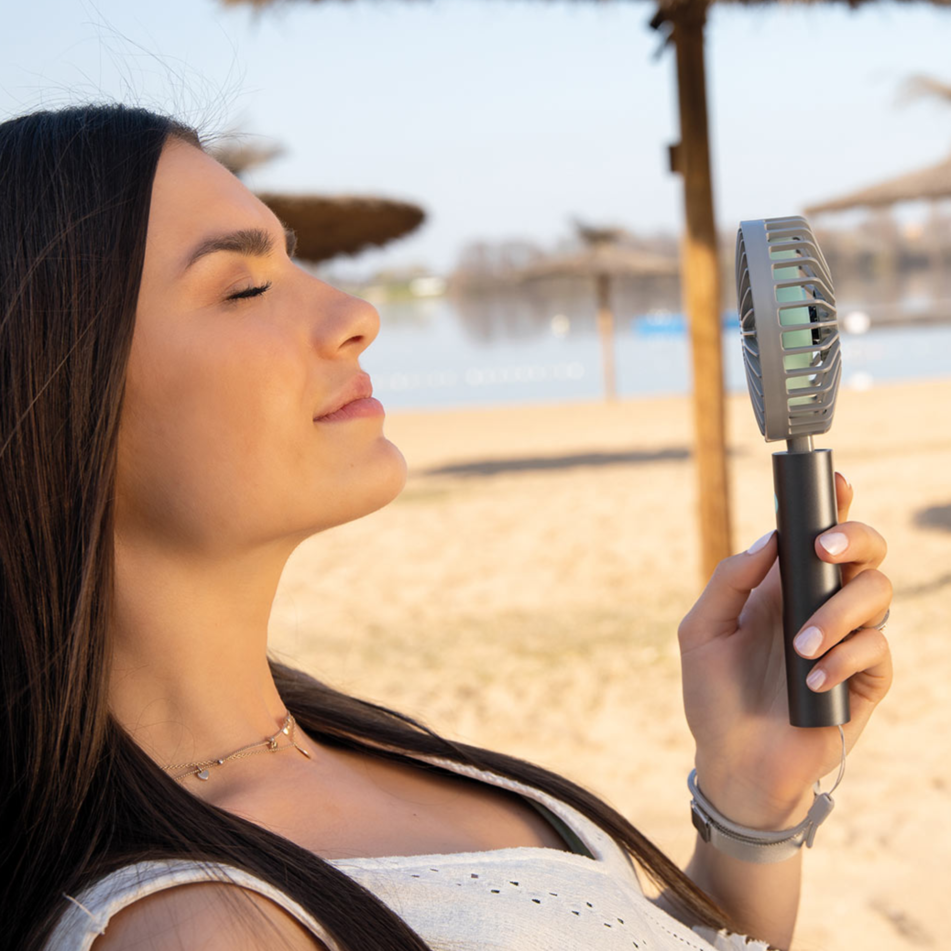 Donna che si gode la brezza di un ventilatore a flusso color grafite sulla spiaggia con gli occhi chiusi.