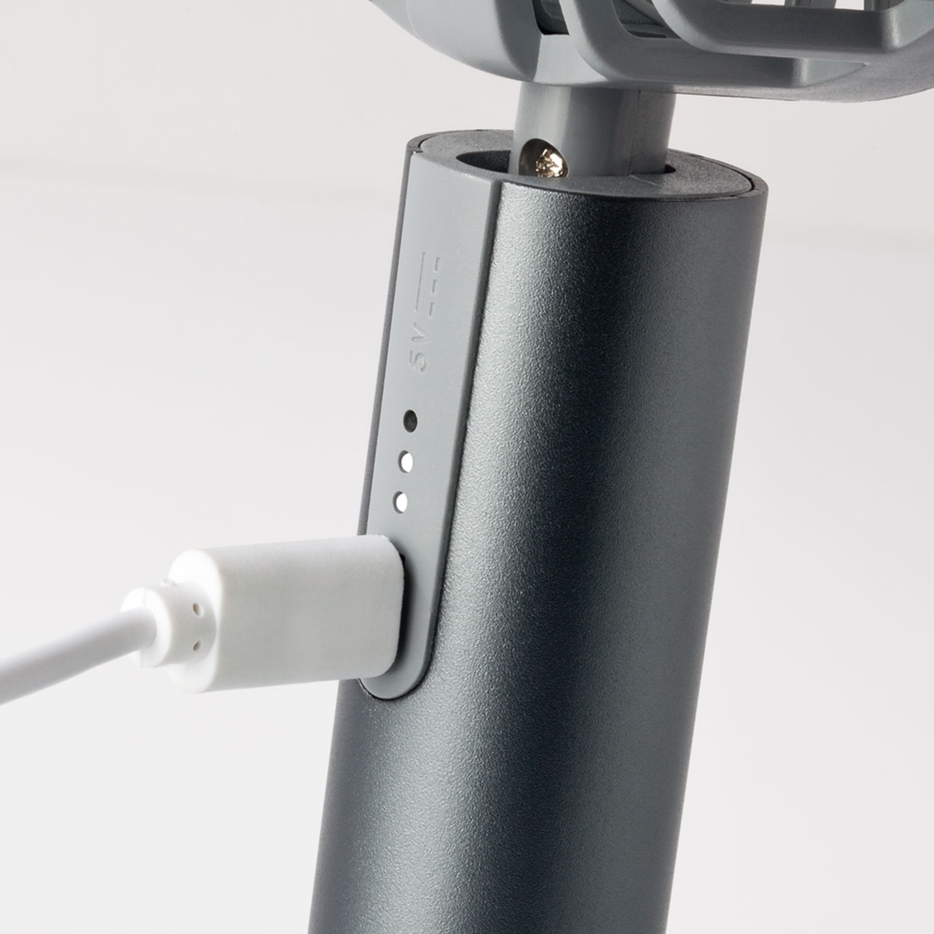 Primo piano del ventilatore Flow 'graphite': cavo USB inserito nell'alloggiamento grigio del ventilatore a batteria, indicatore del livello di carica della batteria accanto.