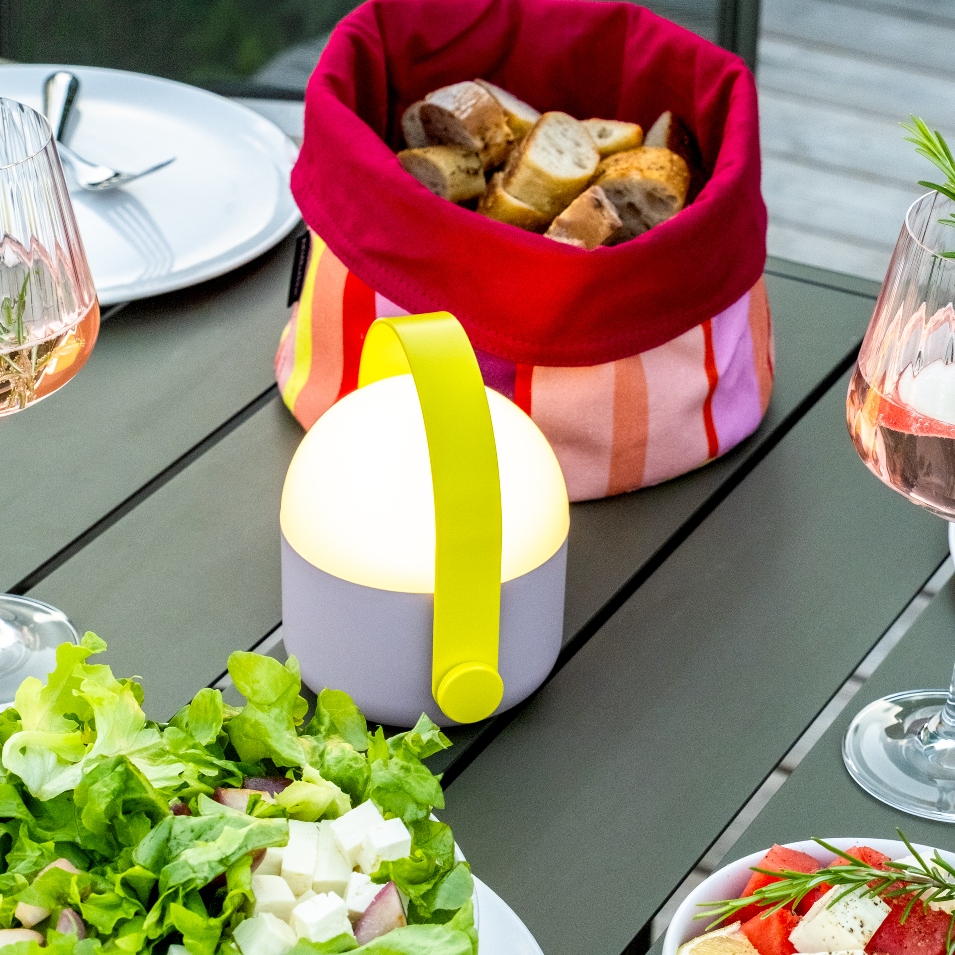 Lampe Ole autonome et portable de couleur lilas avec une anse jaune reliée en haut par un arc. La partie supérieure de la lampe est blanche et s'allume. Sur le côté se trouve un bouton rotatif.