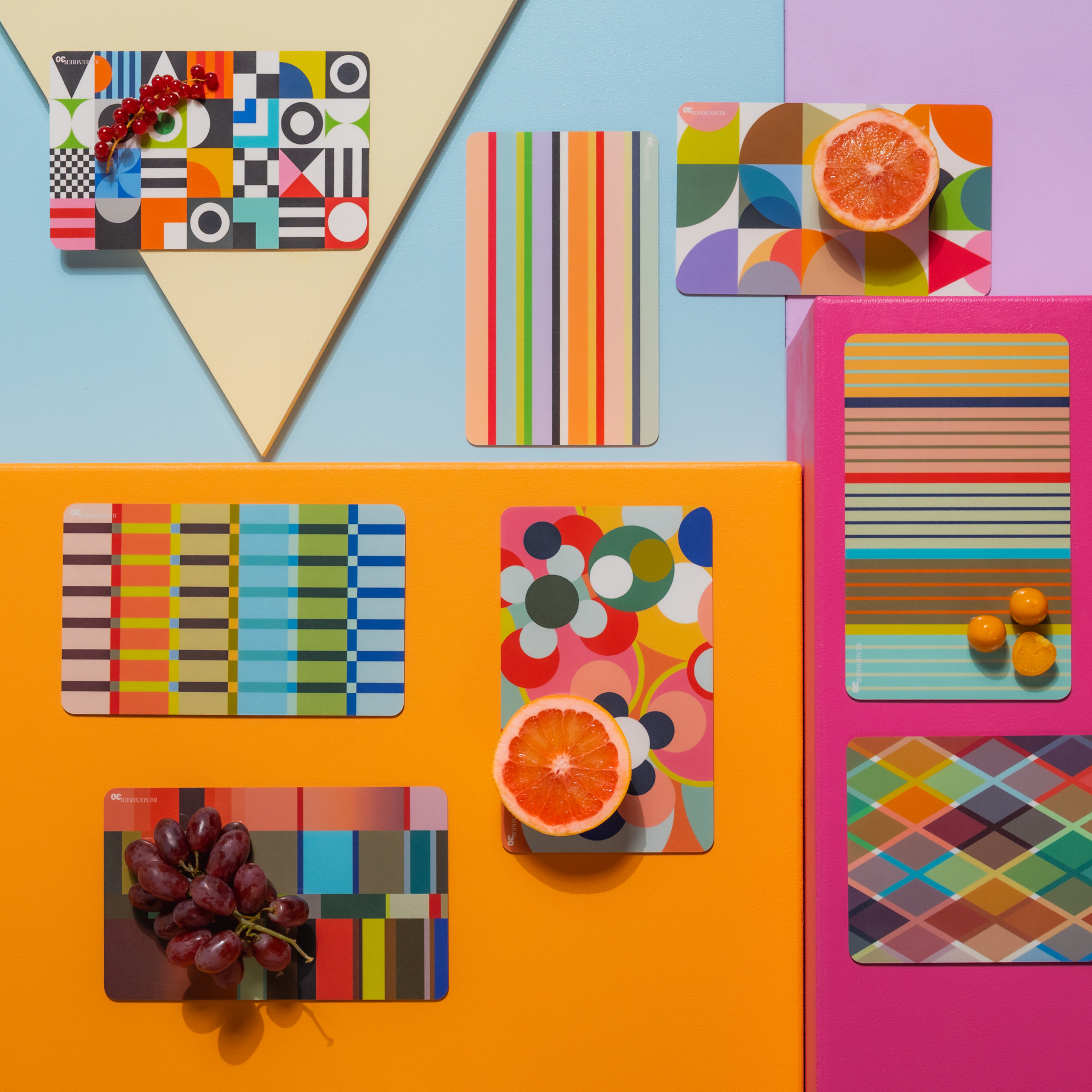 Vibrierende Farbpalette: Geometrische Muster, Streifen und Rauten auf Karten, kuratiert mit frischen Früchten auf farbigem Hintergrund.