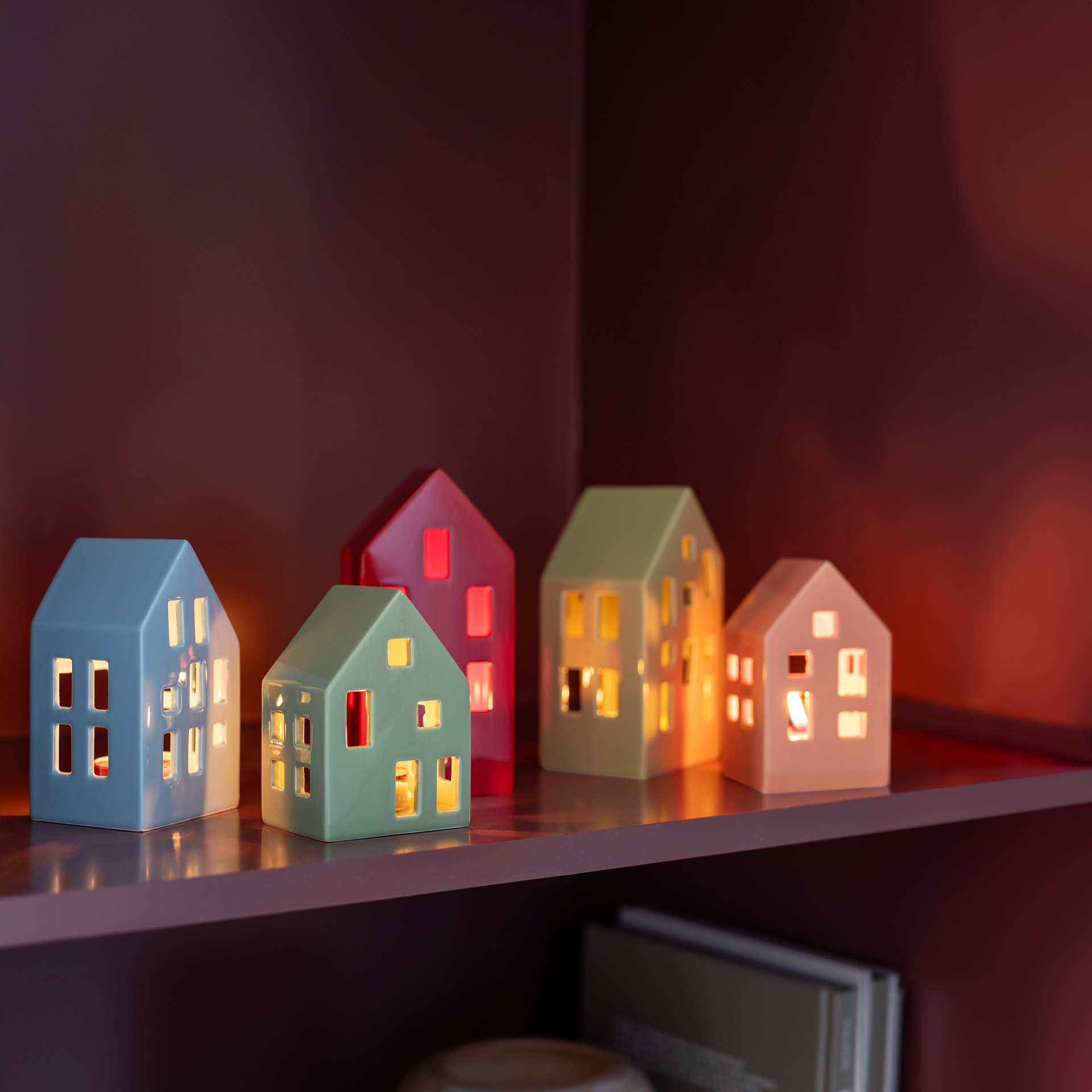 Ein Sortiment bunter Teelichthäuser in Blau, Grün, Rot und Beige steht im Regal, wobei das Licht durch die Fenster scheint.