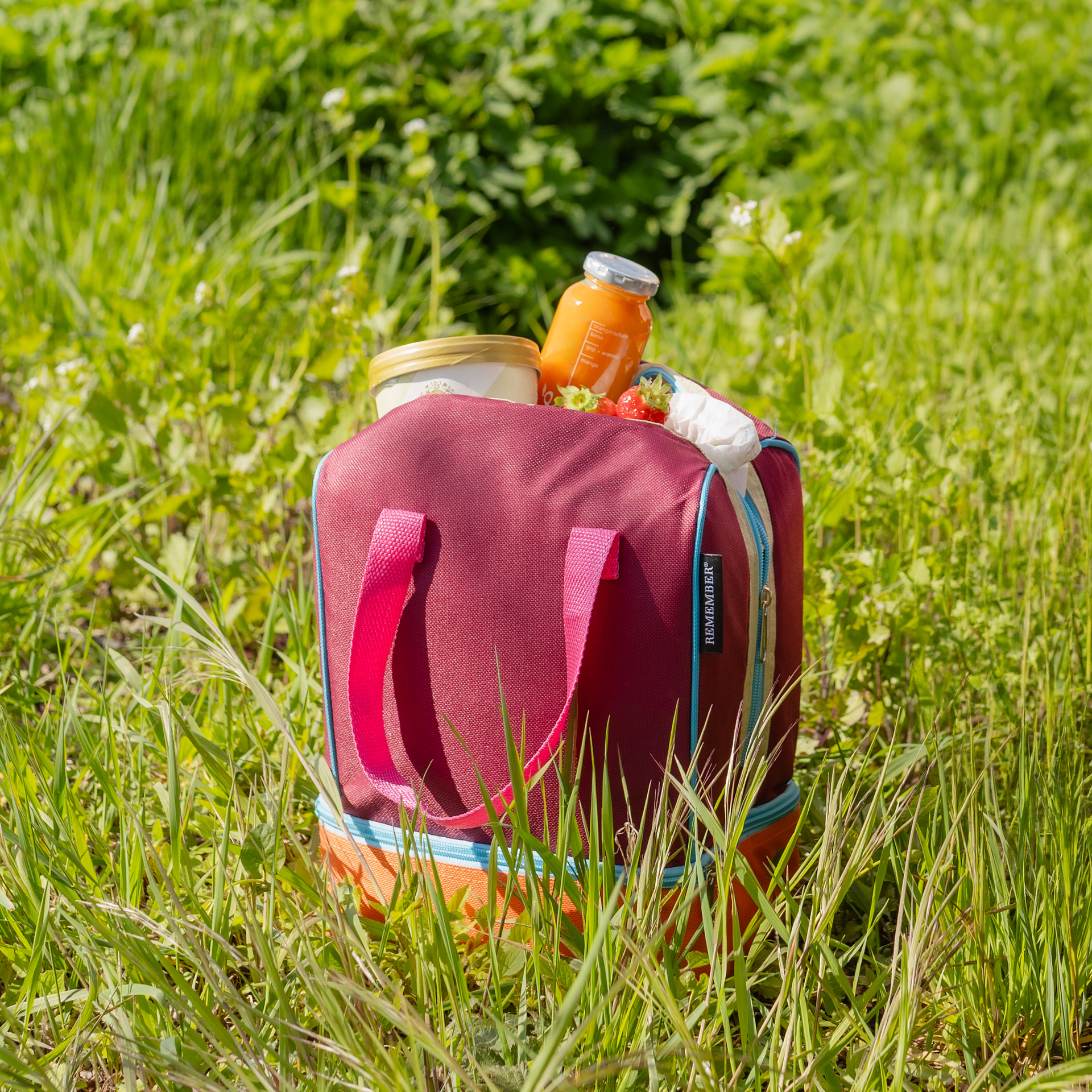 Lunch-Kühltasche 'Telli': Rechteckige Tasche in Aubergine und Orange mit rosa Tragegriffen. Reißverschlüsse und blaue Akzente heben die zwei Fächer hervor.