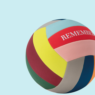 Ein farbenfroher Volleyball mit dem Wort "REMEMBER" in weißer Schrift auf einem roten Feld. Die Ballfelder sind in Gelb, Grün, Rosa, Blau und Grau gehalten. Der Hintergrund ist hellblau.