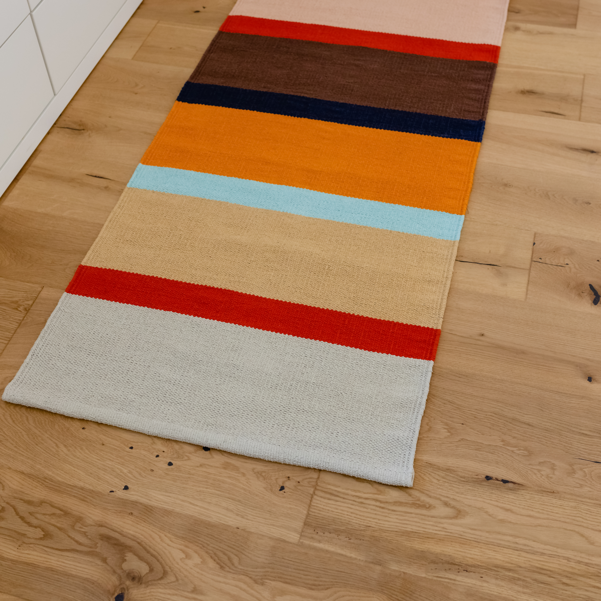Tapis de sol allongé 'Zaza' avec des rayures colorées en beige, bleu, rose, rouge, marron et orange. Coton tissé à la main avec une texture reconnaissable.