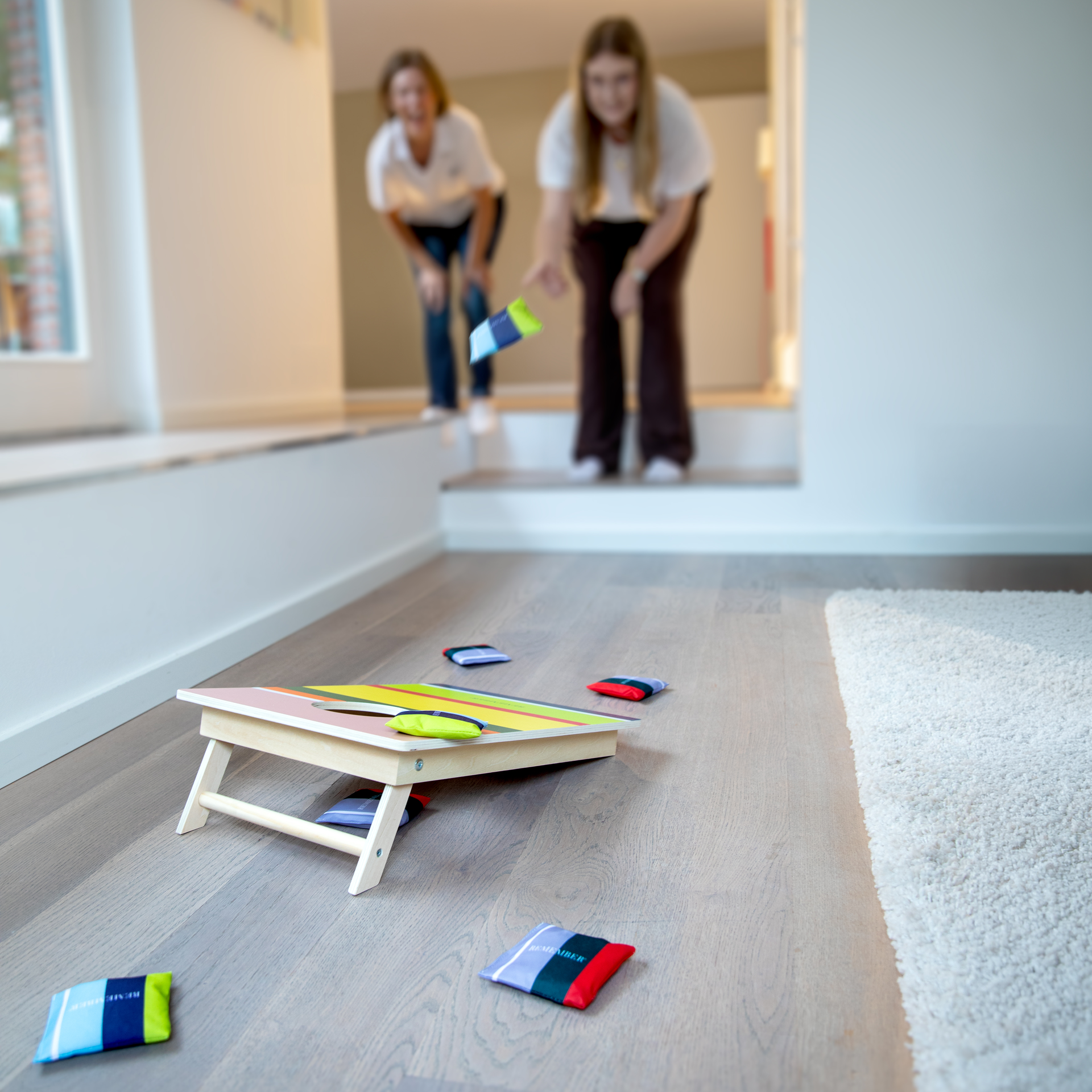 Un tabellone per il gioco del cornhole con quadrati colorati e una buca, circondato da sacchetti da lancio di diversi colori.