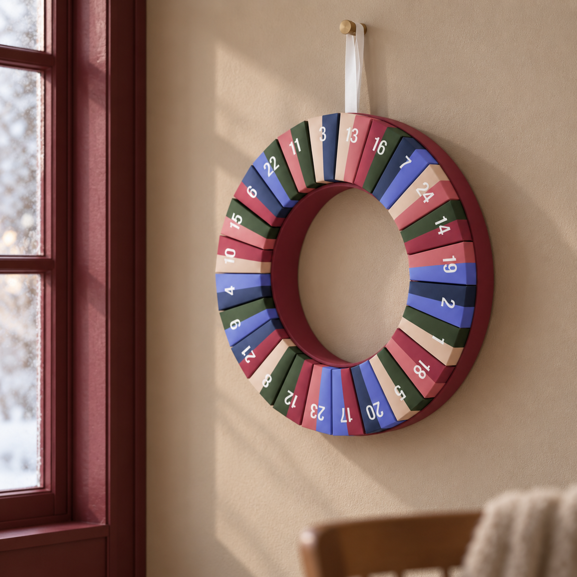 Ghirlanda-calendario dell'Avvento circolare con 24 scomparti numerati in vari colori, tra cui blu scuro, verde scuro, rosa e beige. Appesa a un nastro bianco, con numeri da 1 a 24 distribuiti uniformemente.