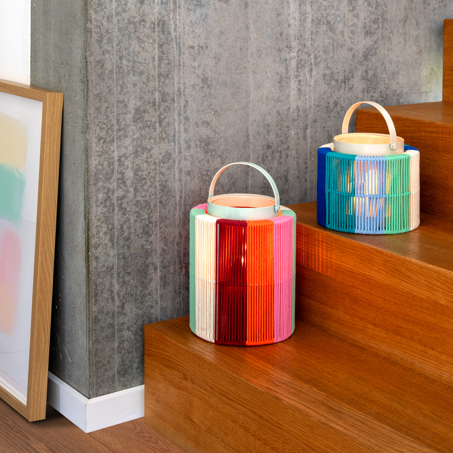 Laterne 'Maja' Sonnenaufgang: Zylindrische Laterne mit Griff, umwickelt mit bunten Baumwollschnüren in Grün, Beige, Rot, Orange und Pink.