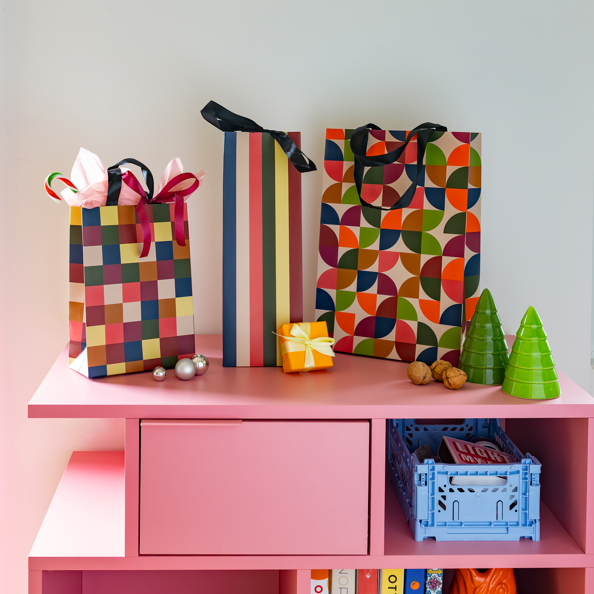 Huit sacs cadeaux colorés avec poignées en ruban satin noir, de tailles variées et en 4 motifs : carreaux, demi-cercles géométriques, rayures horizontales et verticales. Couleurs : rouge, bleu, vert, orange, jaune, rose, marron.