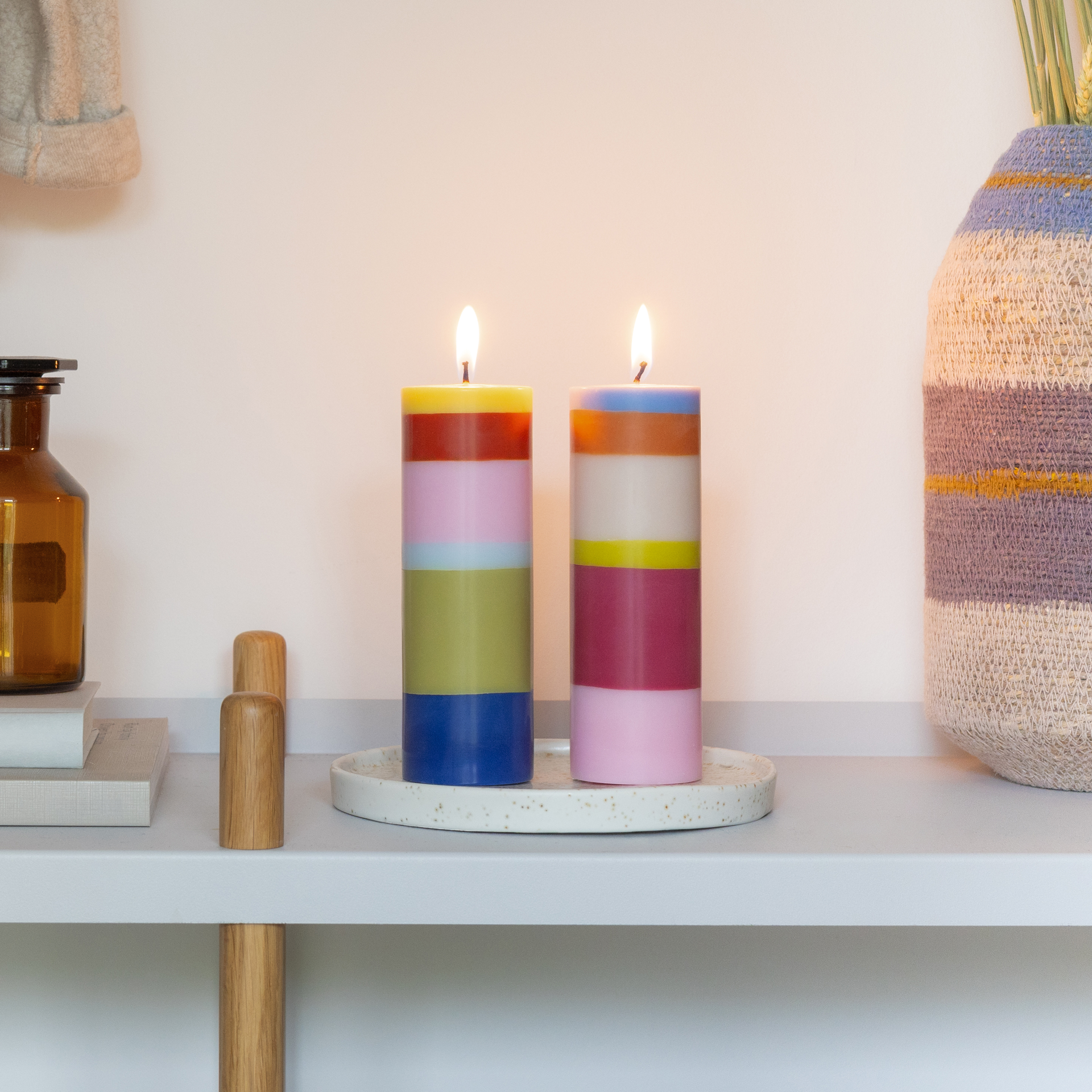Lot de deux grandes bougies cylindriques, chacune avec six couches horizontales. À gauche : vert citron, rouge, rose clair, bleu clair, vert olive, bleu foncé. À droite : bleu clair, orange, beige, jaune, magenta, rose clair.