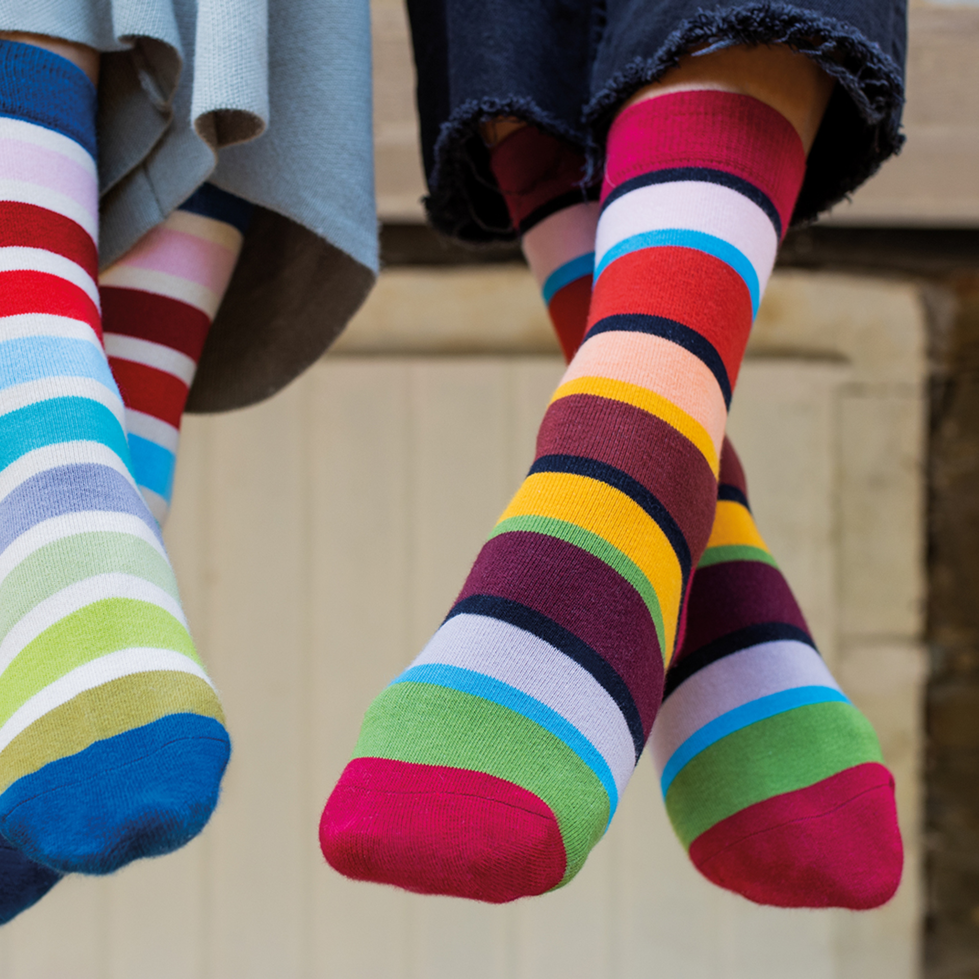 Zwei Personen tragen bunte, gestreifte Socken in den Größen 36-41. Die Socken sind kuschelig weich und warm. Eine Person trägt blaue Jeans, die andere einen grauen Rock.