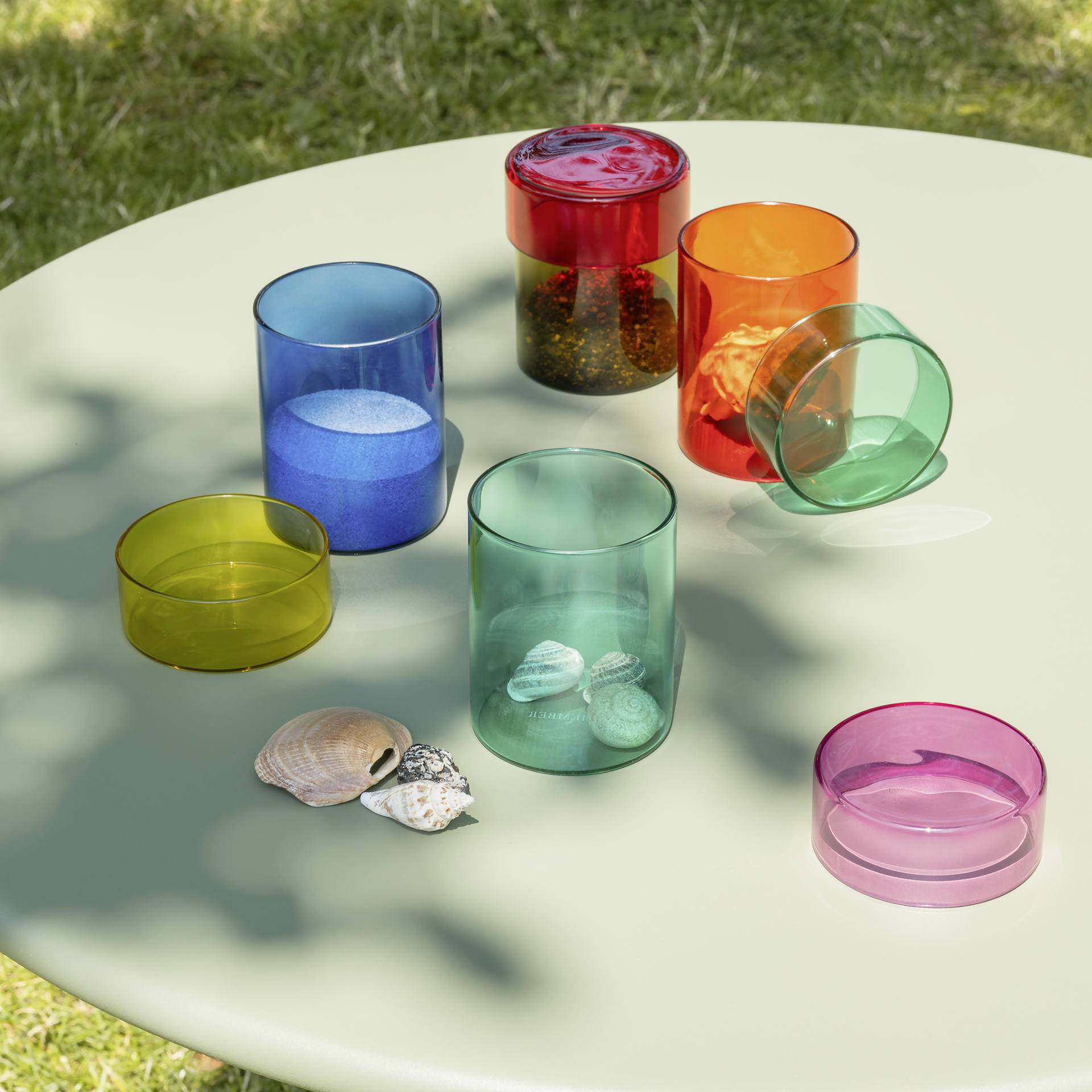 Vier Glasdosen-Sets 'Cosima' in Orange, Türkis, Blau und Gelb mit farblich passenden Deckeln. Jede Dose ist zylindrisch und transparent.