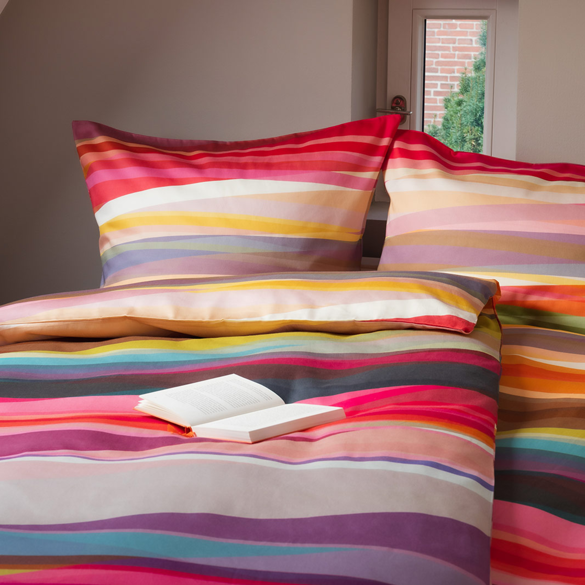 Bettwäsche 'Mateo' aus Mako-Satin, Decke und Kissen liegen übereinander. Das Muster besteht aus bunten, horizontalen Streifen in verschiedenen Farben.