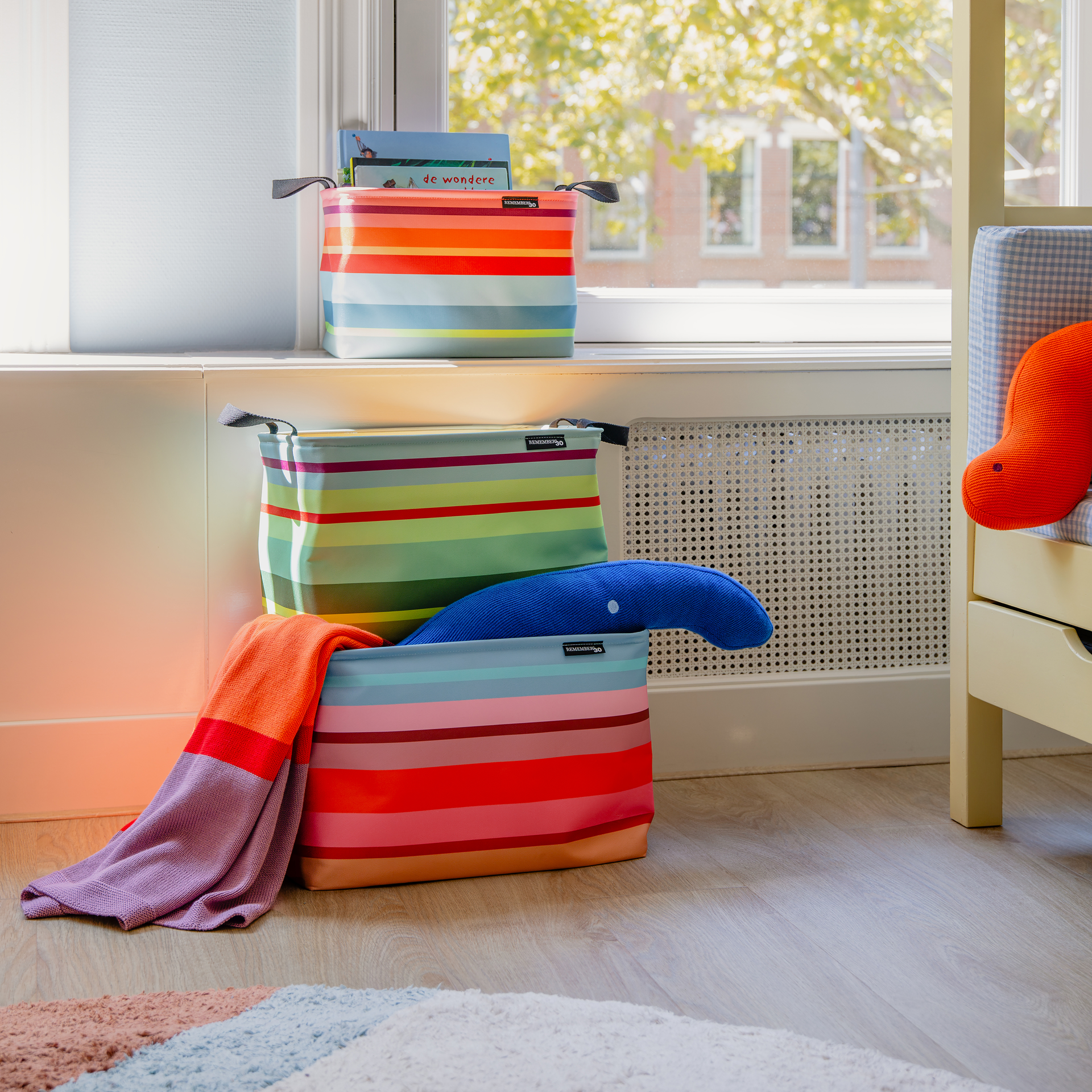 Trois paniers de rangement Nesa empilés, de tailles différentes, ornés de rayures horizontales aux couleurs vives dans les tons de rose, orange, bleu et vert. Chaque panier est muni de poignées noires. À gauche, un fond bleu portant le chiffre 30.