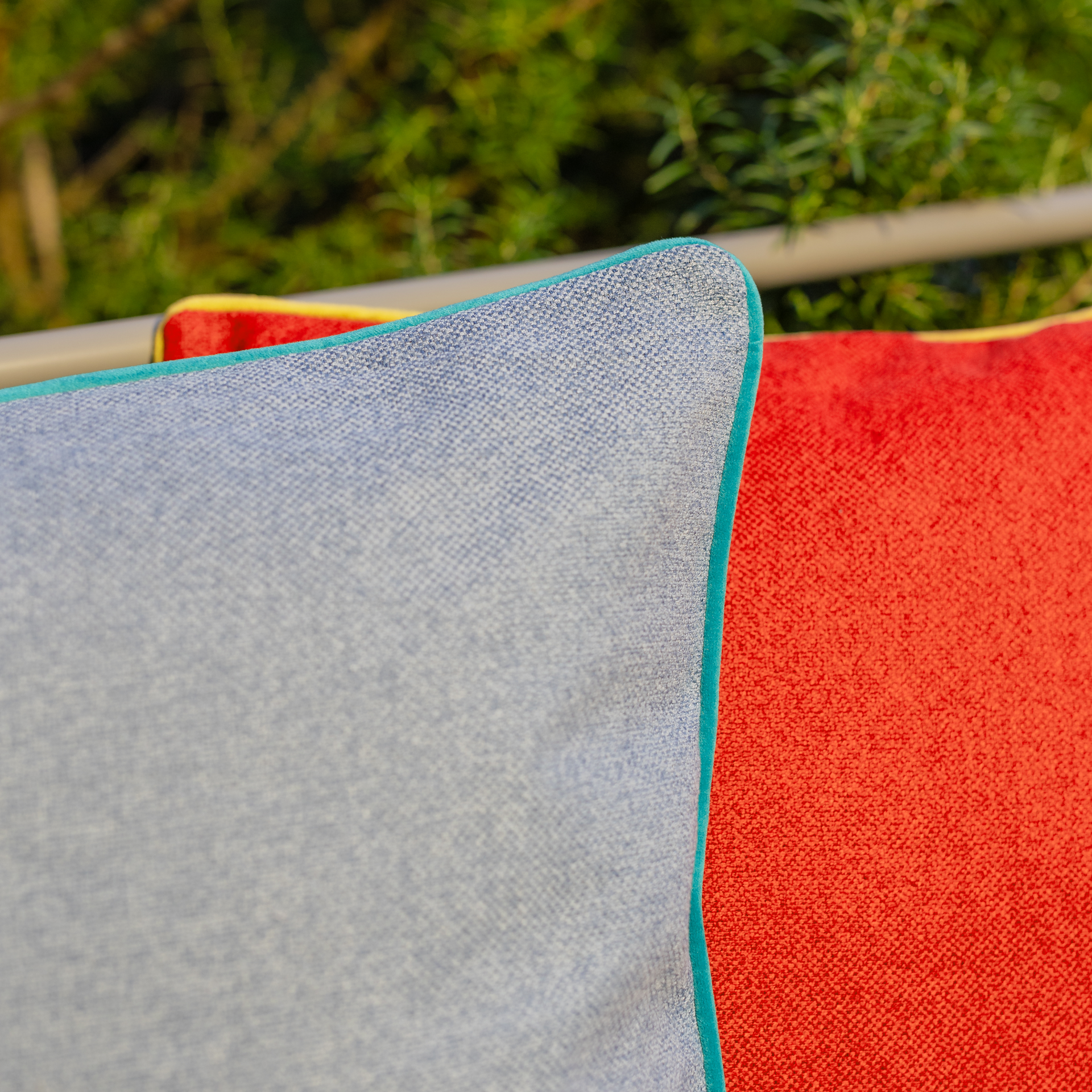 Detailansicht: blaues Kissen mit türkisfarbenem Saum, daneben ein rotes Kissen mit gelbem Saum.