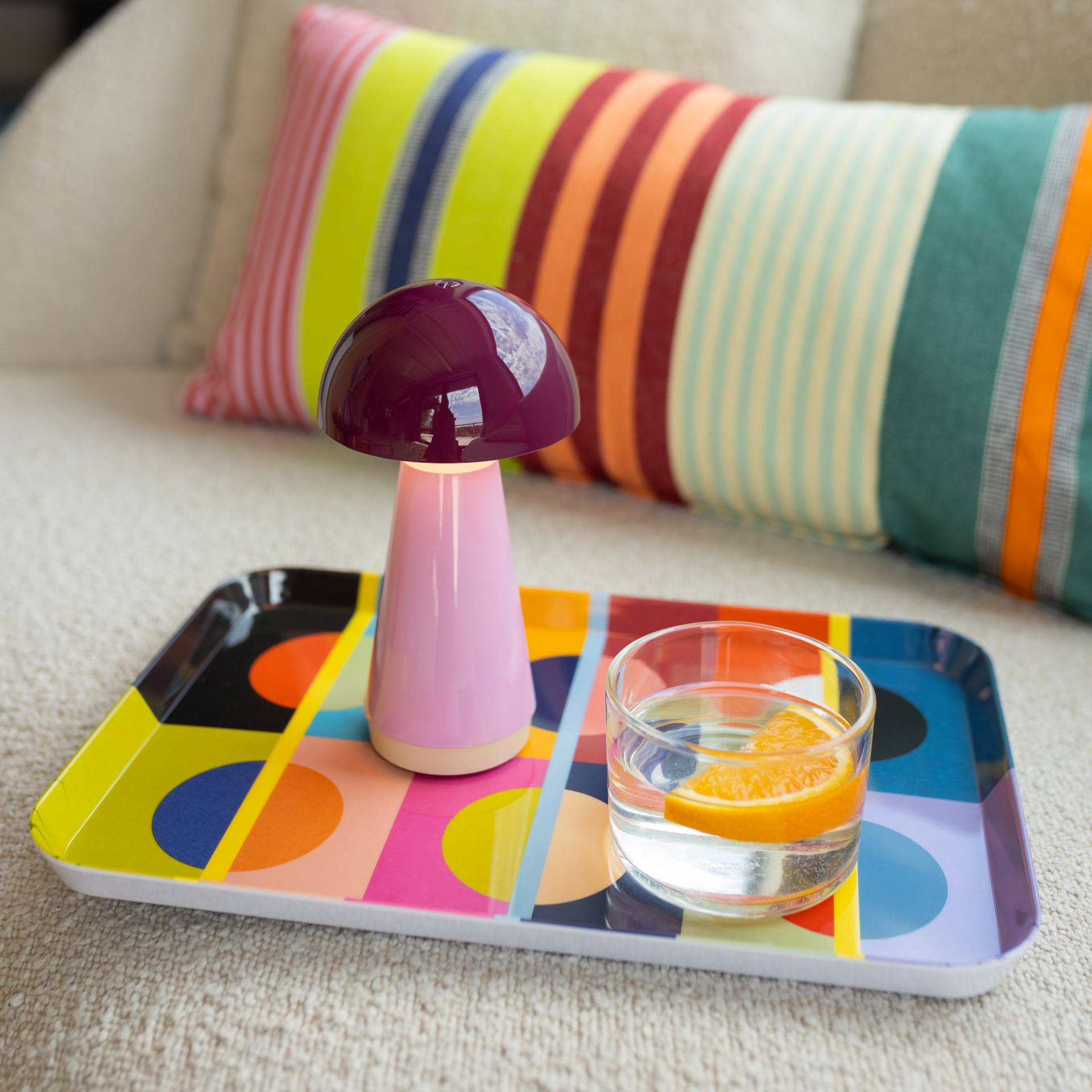 Lampe de table compacte au design champignon sur fond blanc. Tête lumineuse rouge baie brillante, col court blanc. Corps conique rose pâle avec fin bord beige à la base. Lampe LED sans fil Bobbi, dimmable, anti-éclaboussures.