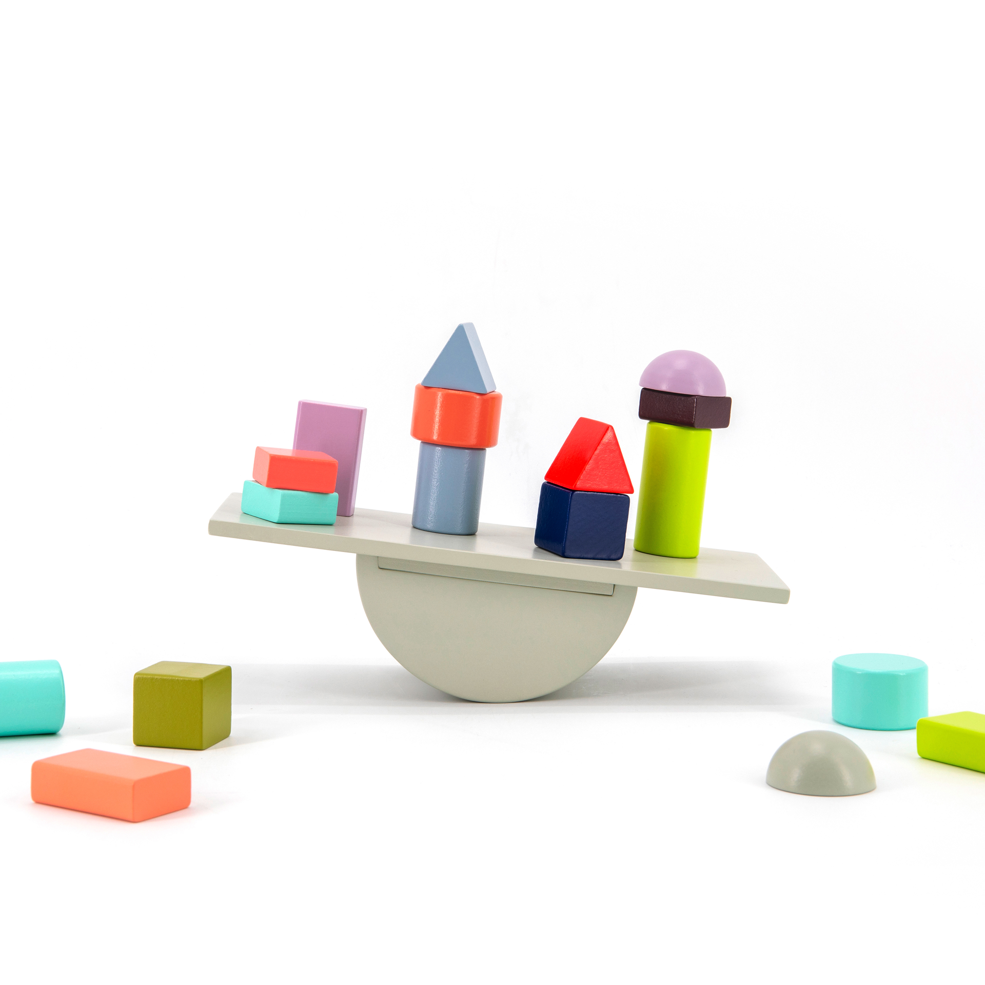 Balancespiel 'Tivoli': Eine hölzerne Wippe mit bunten Bauklötzen in verschiedenen Formen und Farben, einige liegen daneben, vor einem weißen Hintergrund.