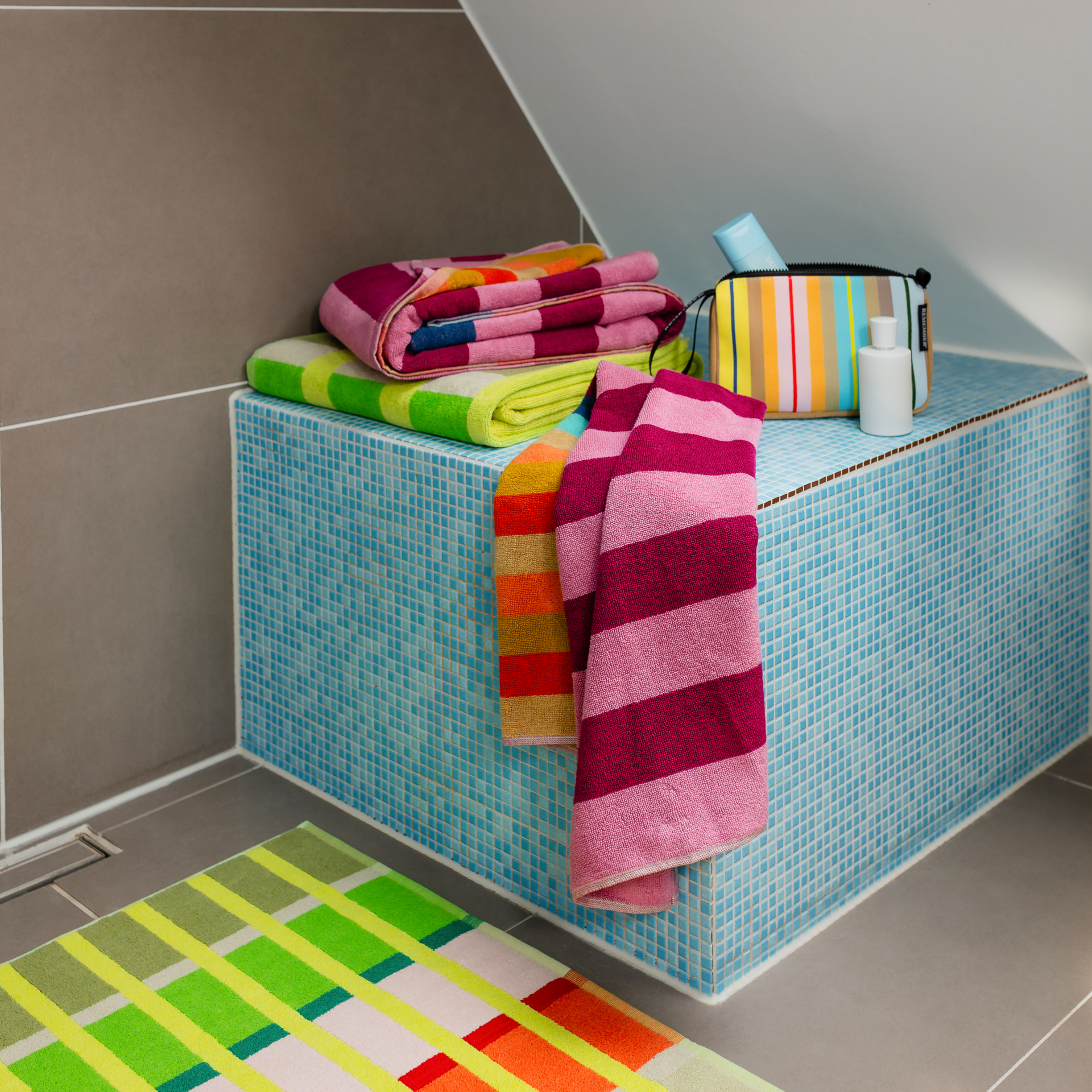 Serviette Alva à rayures horizontales. En haut, tons violets et roses ; au milieu, rayures bleu pétrole et turquoise ; en bas, nuances d'orange clair, beige et orange vif. Motif dynamique et coloré.