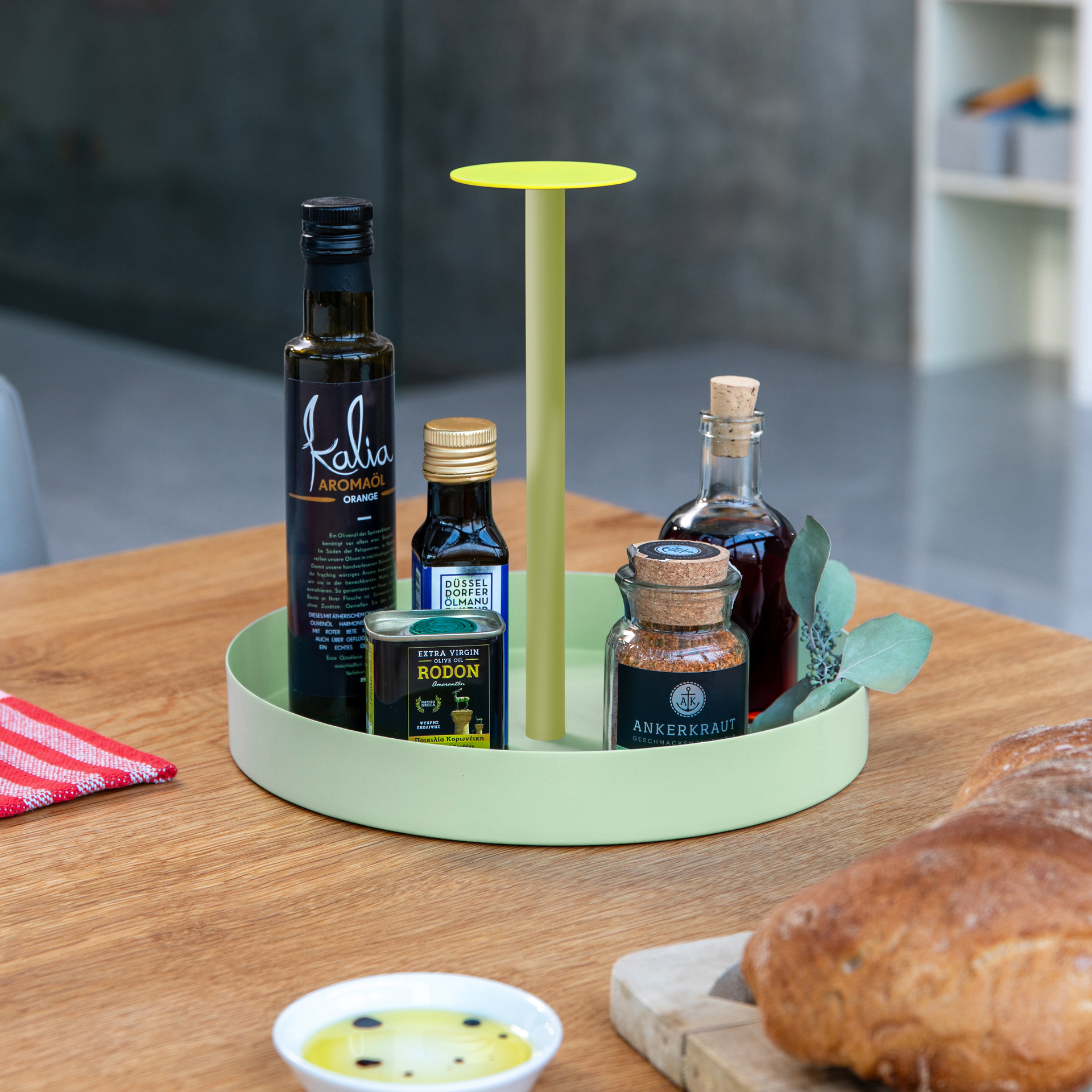 Das limefarbene Tablett 'Nana' mit Griff ist auf einem Holztisch platziert. Darauf sind verschiedene Flaschen und ein Gewürzglas arrangiert, zusammen mit Brot und einer Schale.