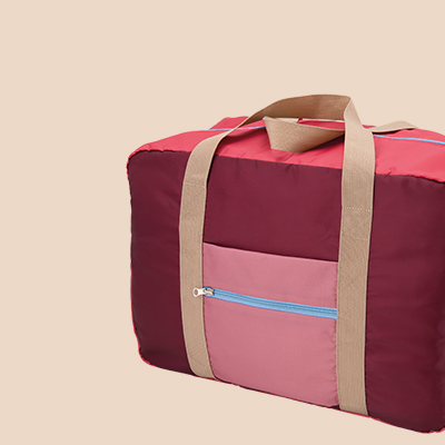 Detailaufnahme einer rosa-weinroten Reisetasche mit beigen Trägern und einer kleinen Fronttasche mit hellblauem Reißverschluss.