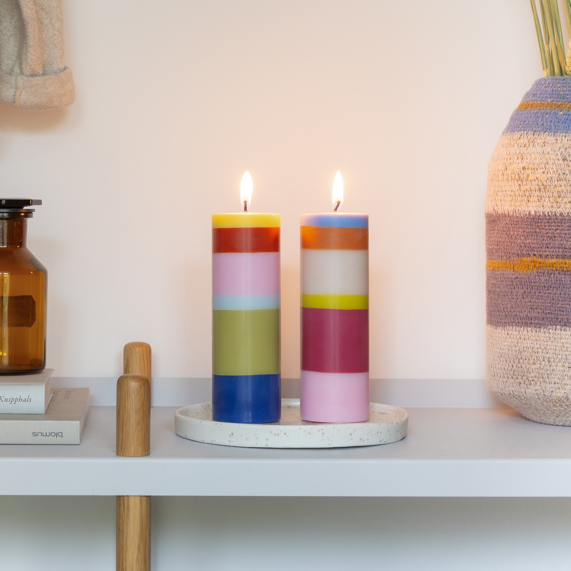 Lot de deux grandes bougies cylindriques, chacune avec six couches horizontales. À gauche : vert citron, rouge, rose clair, bleu clair, vert olive, bleu foncé. À droite : bleu clair, orange, beige, jaune, magenta, rose clair.