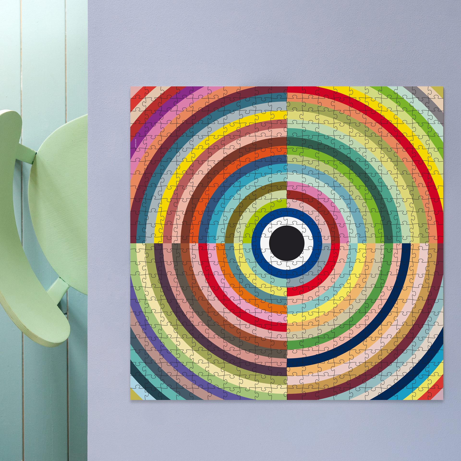REMEMBER Puzzle in zylindrischer schwarzer-blauer Verpackung. Das Mantra-Puzzle zeigt ein Quadrat aus vielen farbigen konzentrischen Kreisen. In der Mitte ein schwarzer Punkt mit weißem Ring, außen Bögen in Blau, Rot, Grün, Gelb.