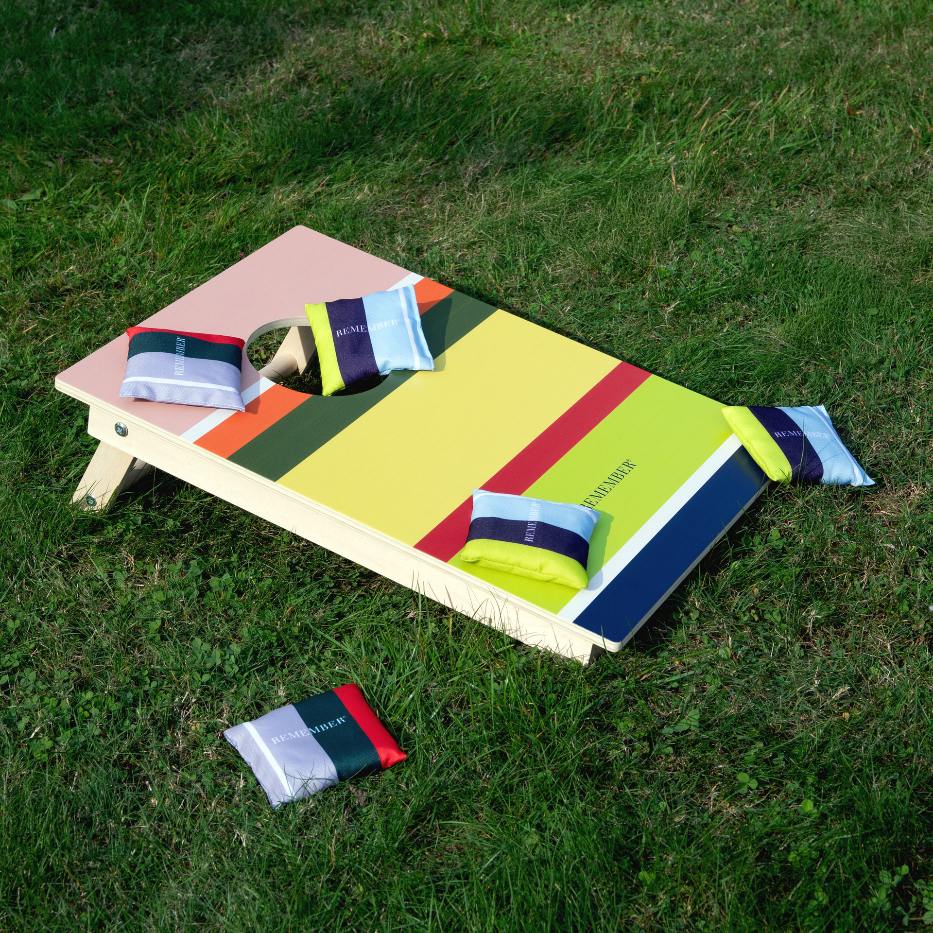 Ein Cornhole-Spielbrett mit farbigen Feldern und Loch, umgeben von Wurfsäckchen in verschiedenen Farben.