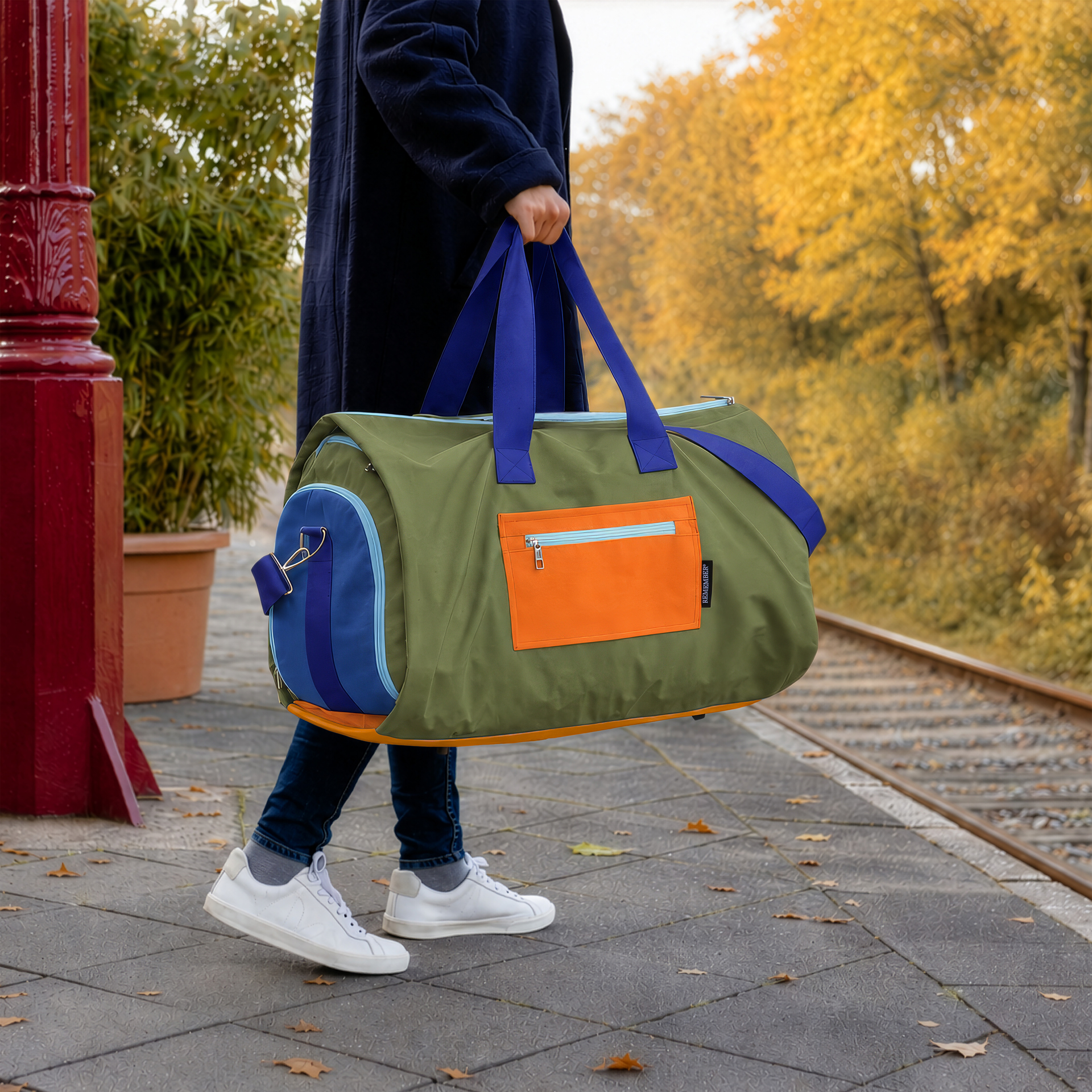 Sac de voyage Lennard vert olive, présenté de profil. Avec des poignées bleues, une bandoulière dotée d'un rembourrage orange et des poches latérales bleu foncé dotées de fermetures éclair bleu clair. Hydrofuge, idéal pour les déplacements.