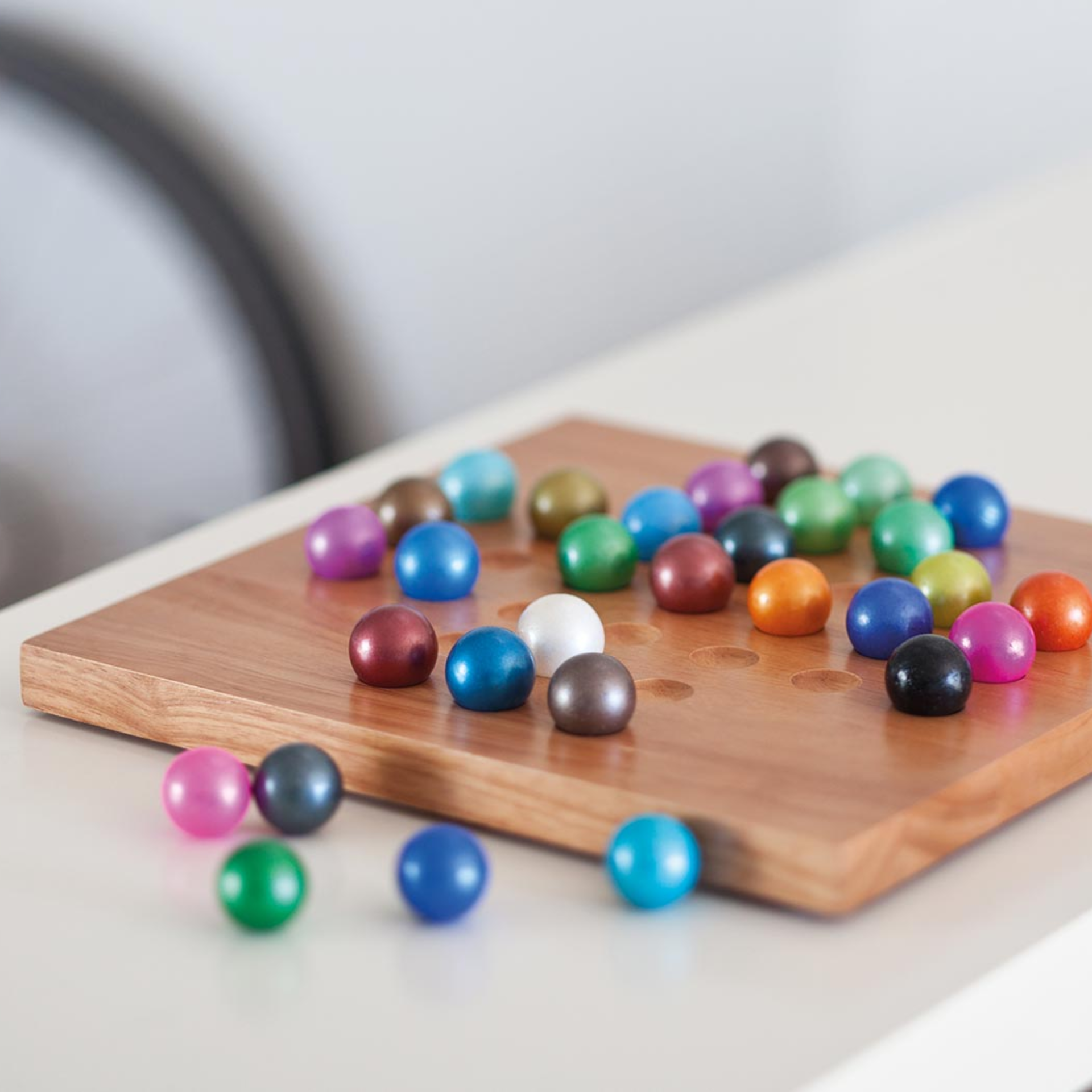 Planche en bois avec des creux, sur laquelle sont posées des billes de verre colorées, certaines étant également dispersées en dehors de la planche. Jeu de solitaire.