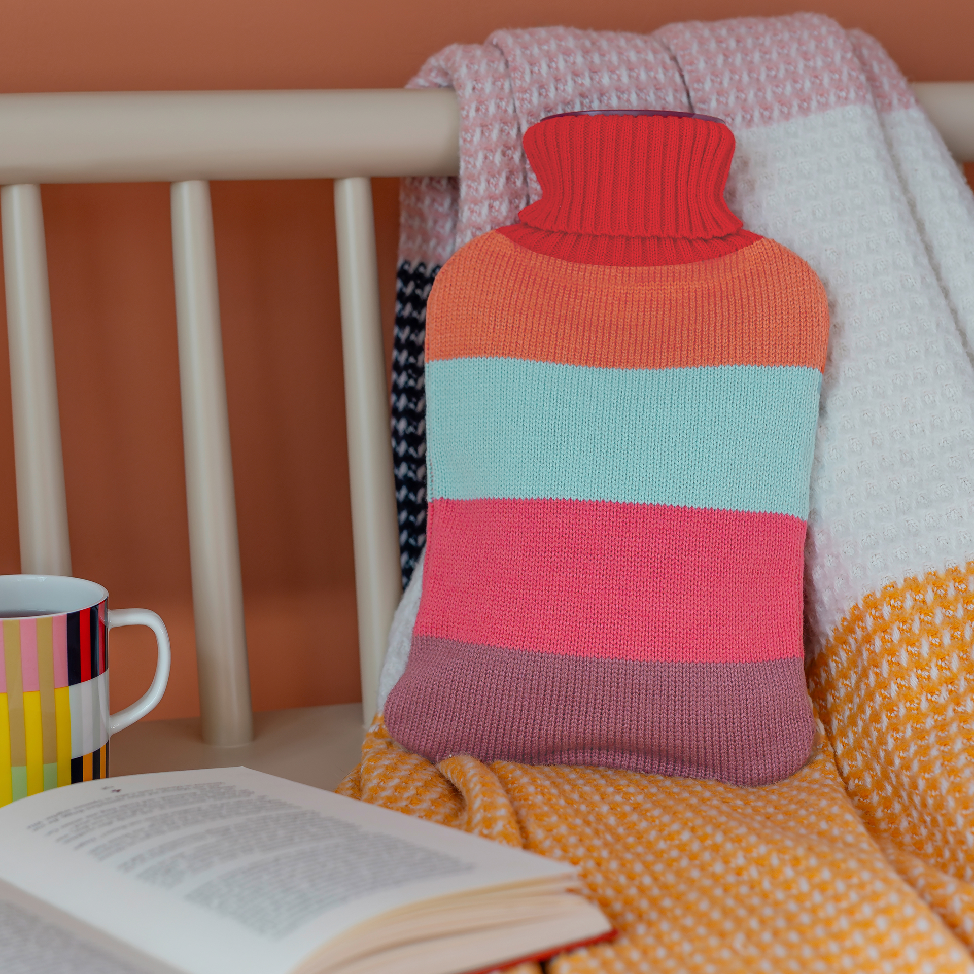 Wärmflasche 'Lilli' mit buntem, gestricktem Cover. Das Design besteht aus Streifen in Orange, Türkis, Rosa und Lila. Der Hals ist rot gestrickt.