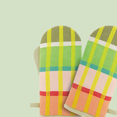 Zwei Topfhandschuhe mit Karomuster in Grün-, Gelb-, Rosa- und Rottönen. Die Handschuhe liegen nebeneinander auf einem hellgrünen Hintergrund.