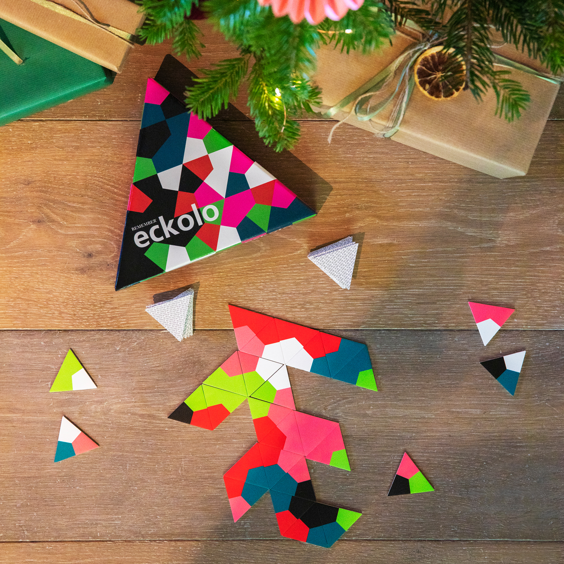 Eckolo Spiel: Dreieckige Karten, Box mit geometrischem Muster und Geschenke auf Holztisch unter einem Weihnachtsbaum.