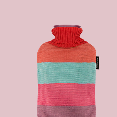 Eine Wärmflasche mit einem gestrickten Cover in horizontalen Streifen. Die Farben sind Rot, Orange, Türkis, Rosa und Lila. Der Hals ist rot gestrickt.