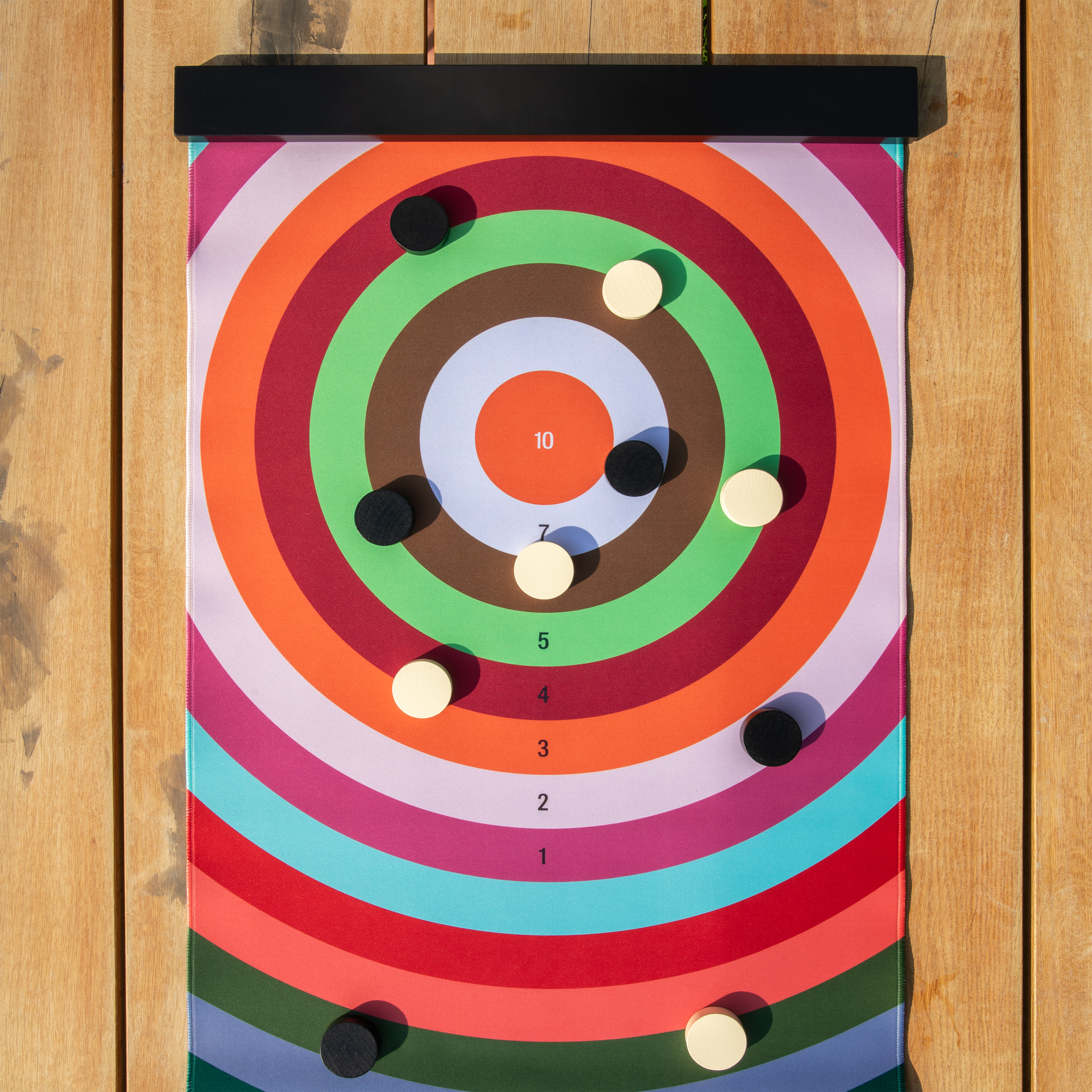 Dartscheibe mit farbigen Ringen und Punktzahlen, an der schwarze und weiße Spielsteine befestigt sind. Die Dartscheibe hängt vor einer Holzwand.