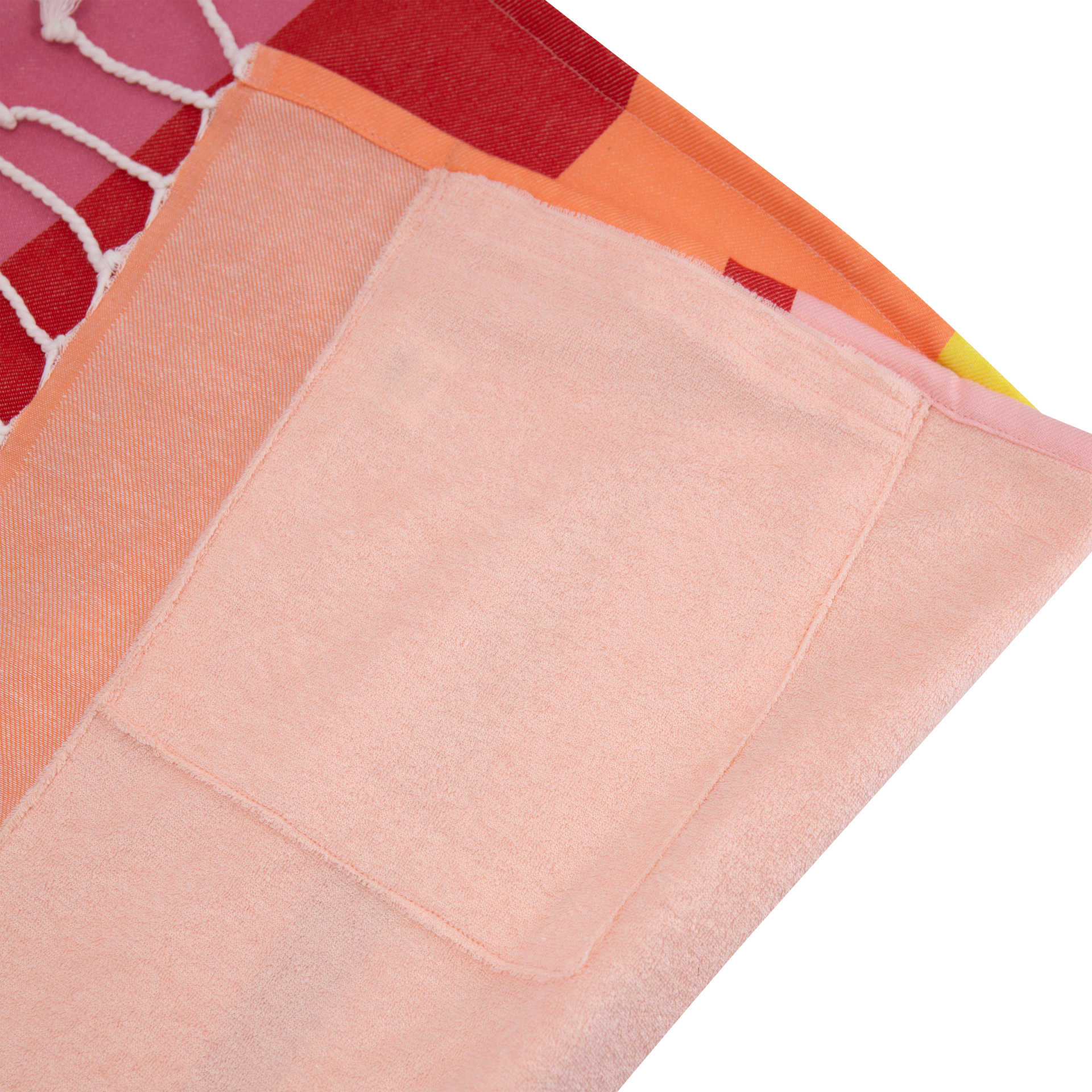 Ein farbenfrohes, gefaltetes Stoffstück mit Fransen, bestehend aus rot-orange karierten Elementen und einem einfarbigen, hellpfirsichfarbenem Tuch mit einer aufgenähten Tasche.