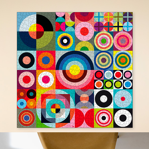 Grand puzzle assemblé, décoré d’un motif géométrique abstrait très vivant. Il présente de nombreux carrés avec des cercles colorés, anneaux concentriques, demi-cercles et quarts de cercle en rouge, bleu, vert, jaune, rose et noir.