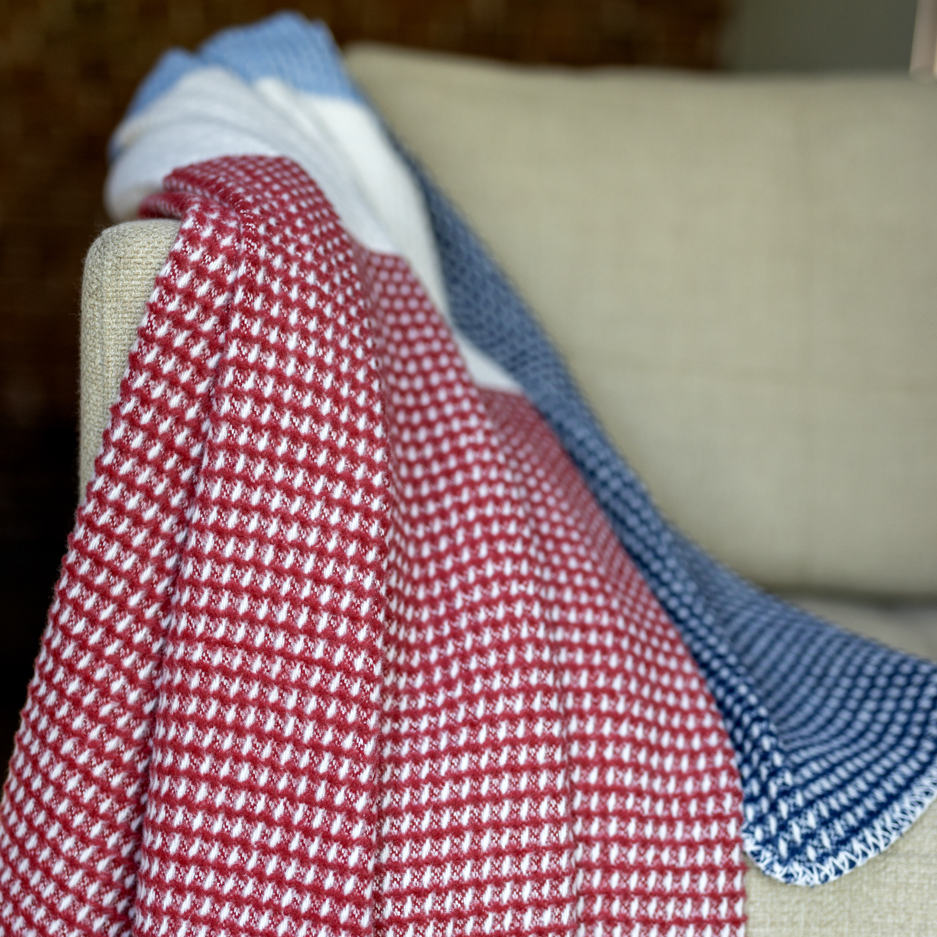 Detailaufnahme einer 'Malie' Couchdecke in Rot, Weiß und Blau mit Waffelmuster über einem Sofa drapiert.