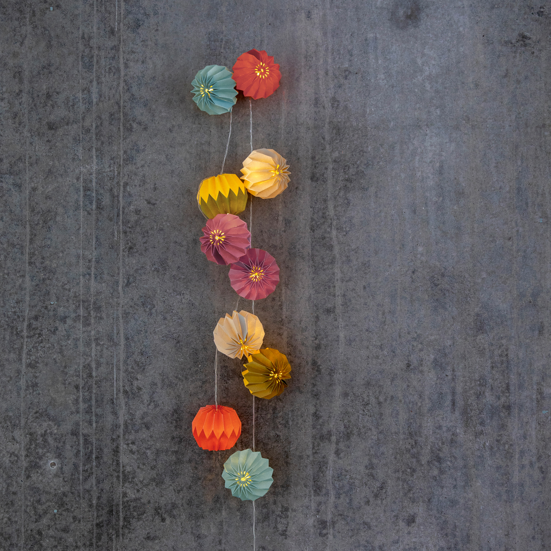 Eine Papier-Lichterkette Yazz mit zehn farbigen, kugelartigen Ornamenten, die von einer Lichterkette gehalten werden. Die Papierlaternen sind beleuchtet.