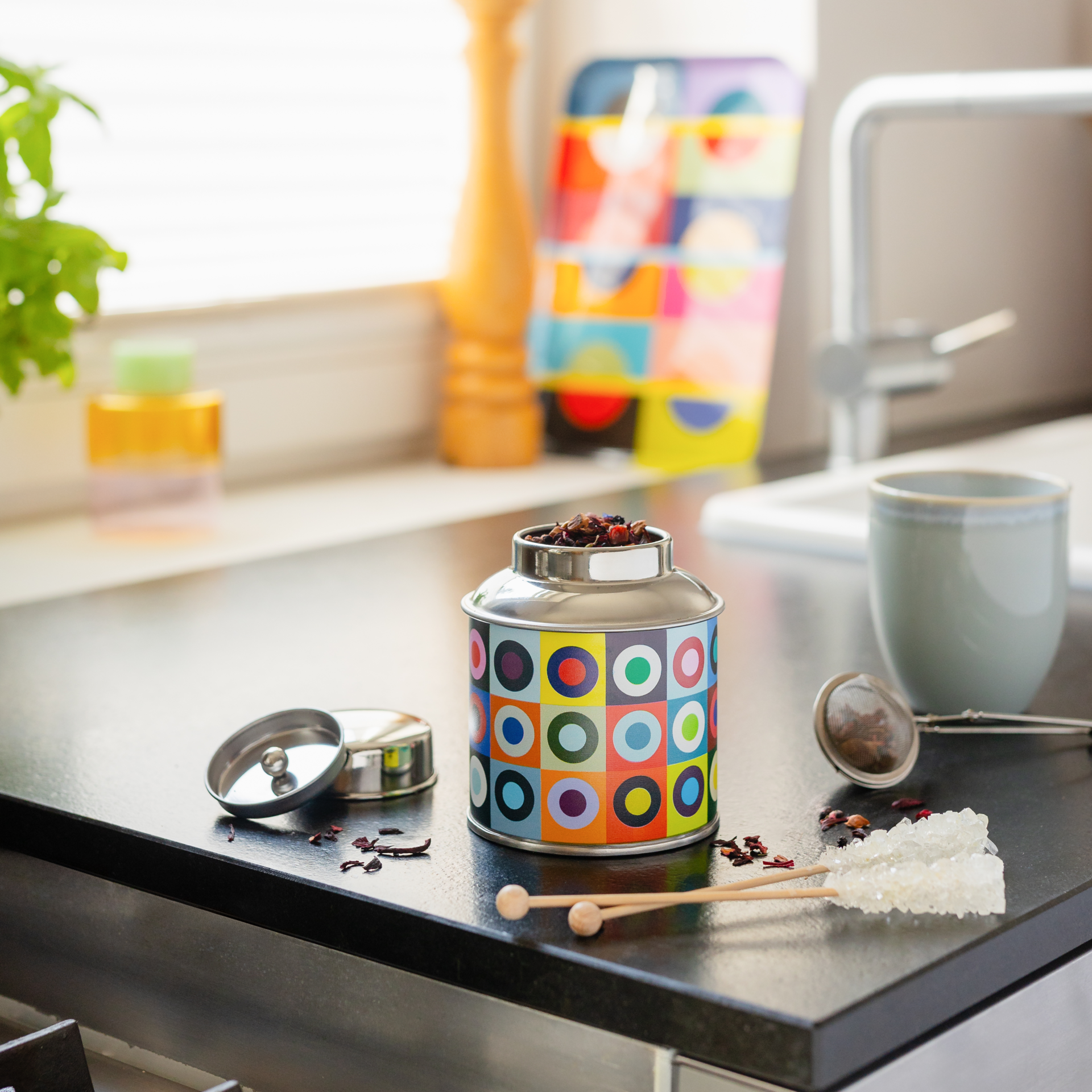 Scatola da tè rotonda in acciaio inossidabile con un vivace motivo a quadrati multicolori e cerchi concentrici colorati. Coperchio lucido color argento. Ideale per conservare il tè, chiusura ermetica che mantiene fresco il contenuto.