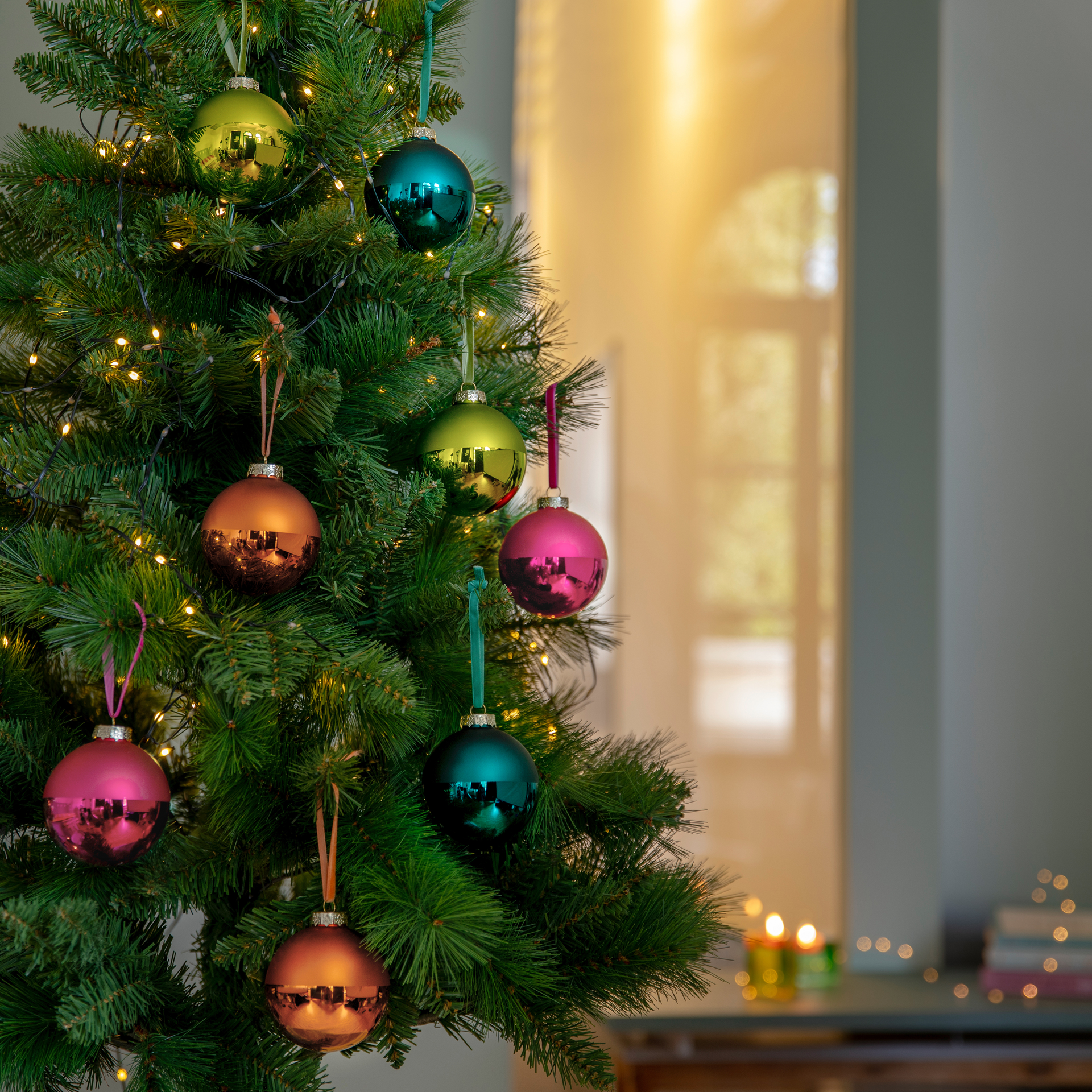 Vier Weihnachtskugeln in Rot, Türkis, Orange und Grün. Die obere Hälfte ist matt, die untere glänzend.