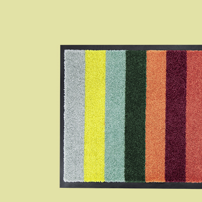 Rechteckige Fußmatte mit breiten, senkrechten Streifen in Grau, Gelb, Türkis, Grün, Orange, Weinrot und Rostrot, umrandet von einem schmalen, schwarzen Rand.