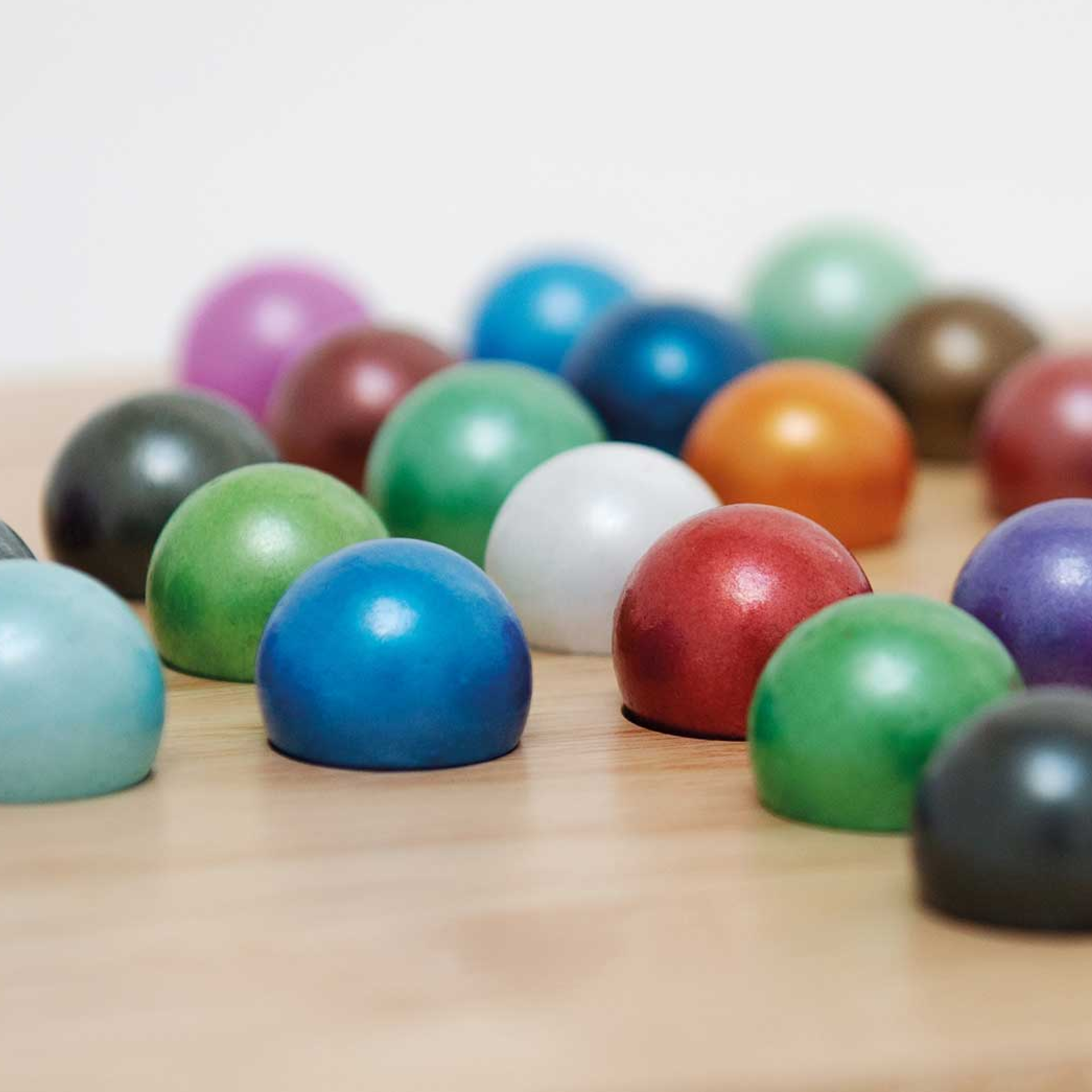 Gros plan de billes de verre colorées du jeu Solitaire sur un fond en bois clair. Les billes brillent de différentes couleurs.