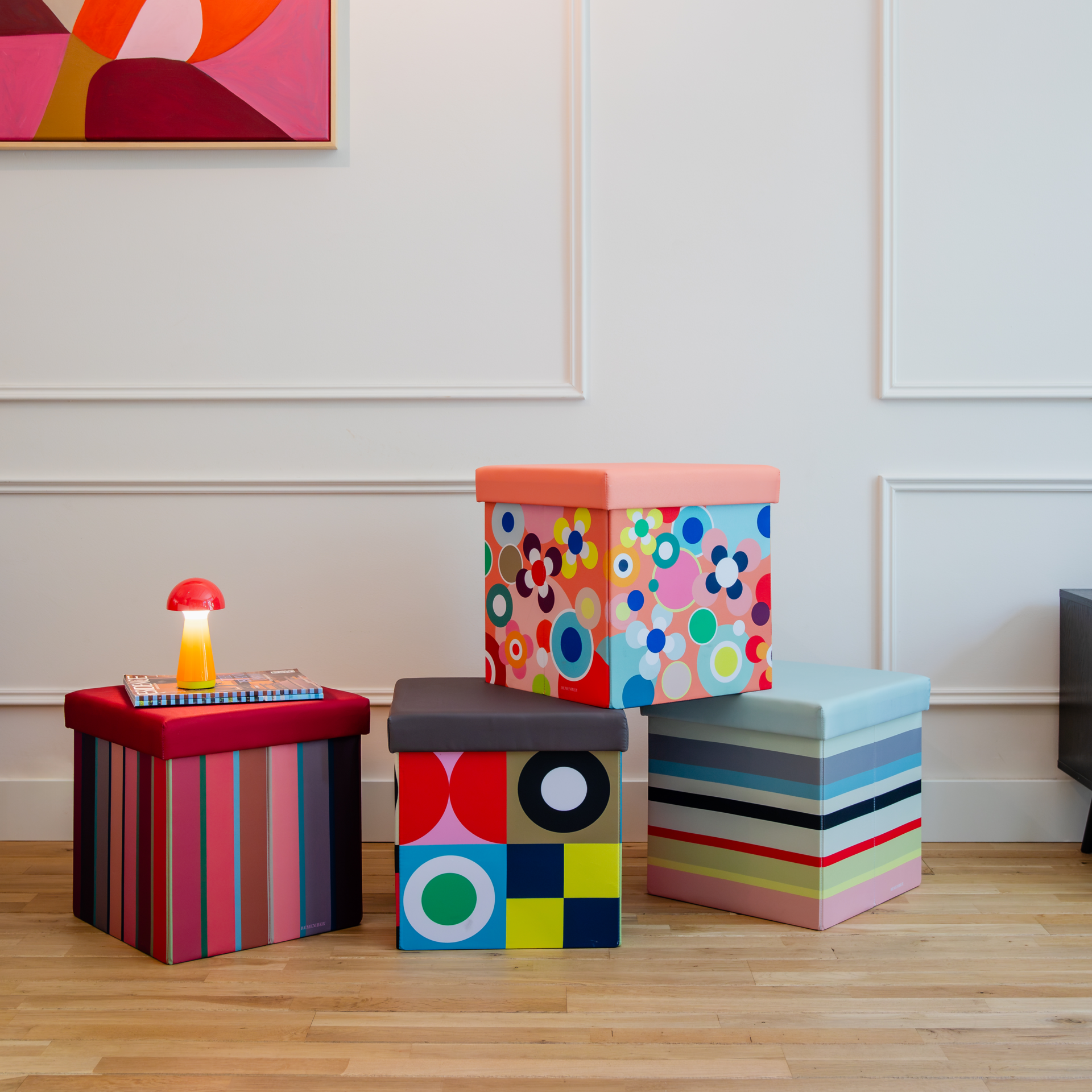 Boîte-siège cubique avec couvercle rembourré rouge foncé. Côtés à motif de rayures verticales vives : rouge, rose, orange, marron, bleu et vert. En haut à gauche, étiquette bleue « Remember 30 » avec « 30 » multicolore.