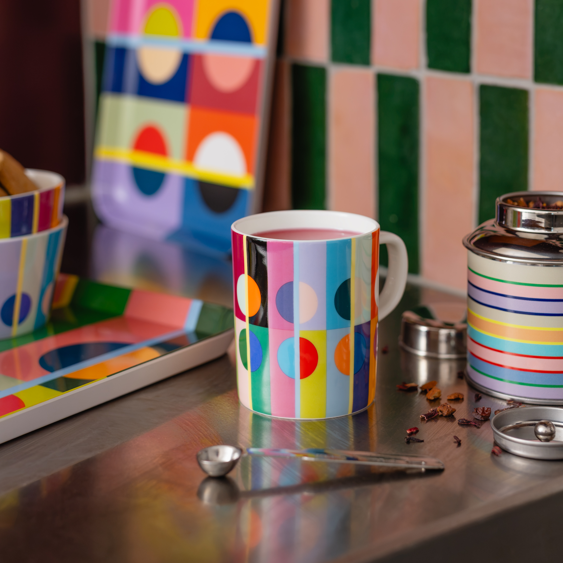 Farbenfrohe Orb-Tasse aus Porzellan mit auffälligem geometrischem Muster: breite vertikale Streifen in Pink, Blau, Gelb, Grün und Orange. Darüber große Kreise in Schwarz, Weiß und Rot, teils überlappend. Weißer Henkel.