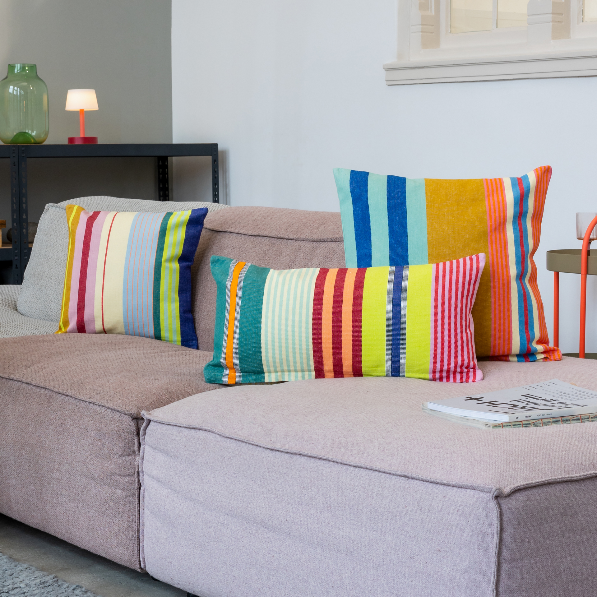Rechteckiges Baumwoll-Kissen 'Grenada' mit bunten Streifen in Grün, Orange, Blau, Gelb, Rosa und Weiß auf weißem Hintergrund.