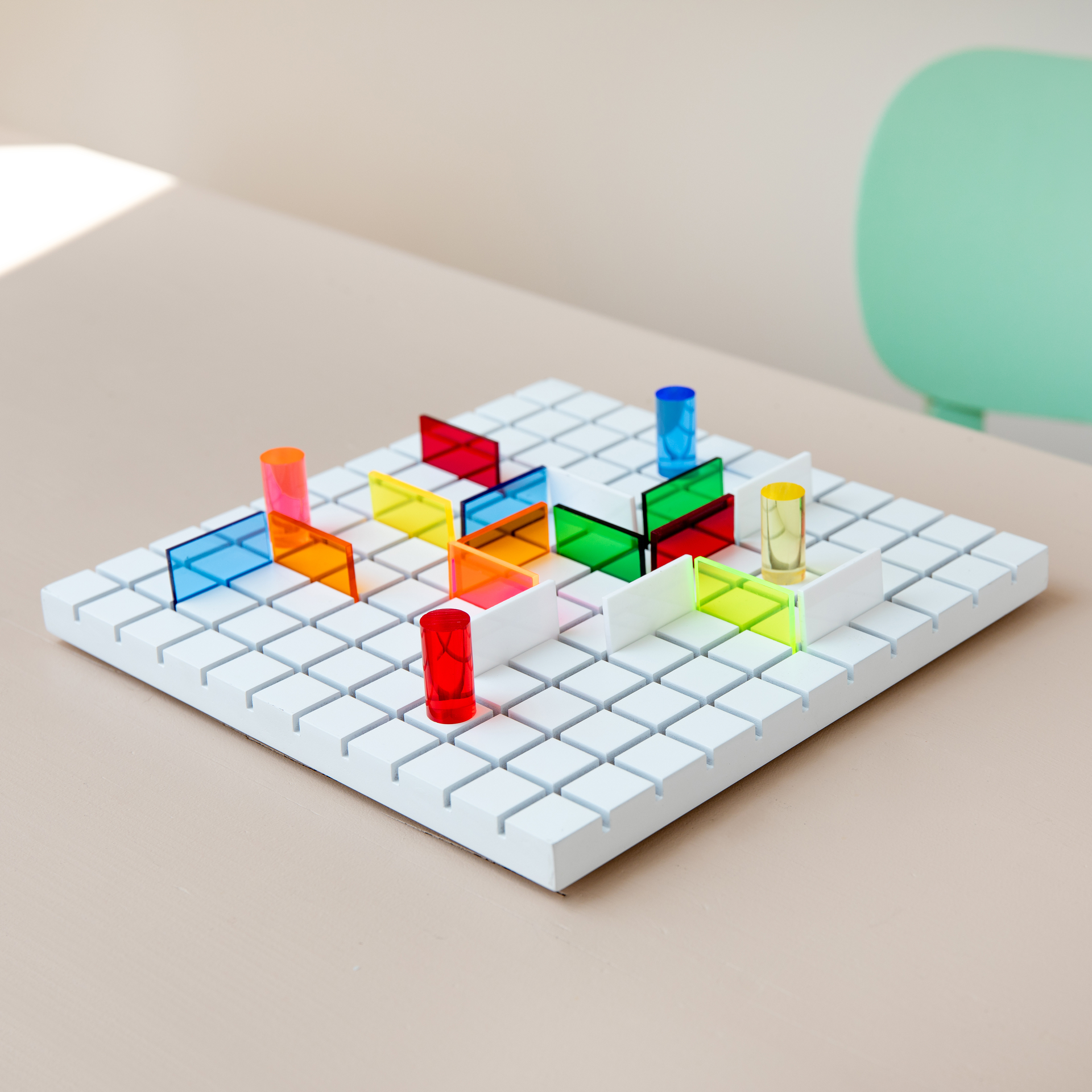 Taktikspiel Paso: Weißes Spielbrett mit farbigen Hindernissen und Spielfiguren in rot, blau, gelb und orange. Quadratische Felder bilden den Untergrund.