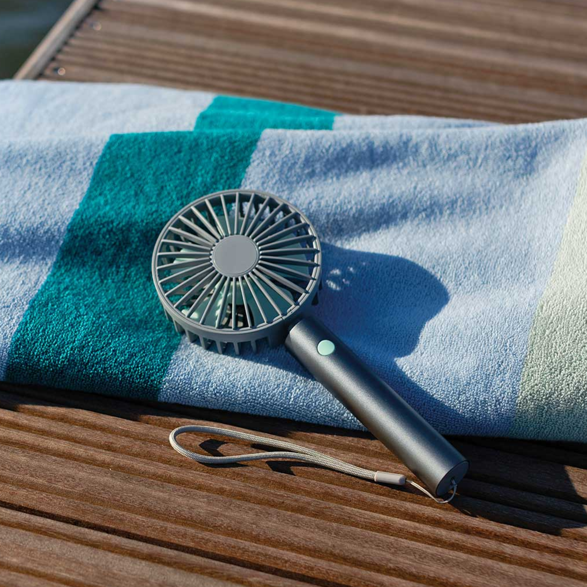 Ventilateur à main rechargeable de couleur graphite avec des pales turquoises et un bouton sur la poignée, dégagé sur un fond blanc.